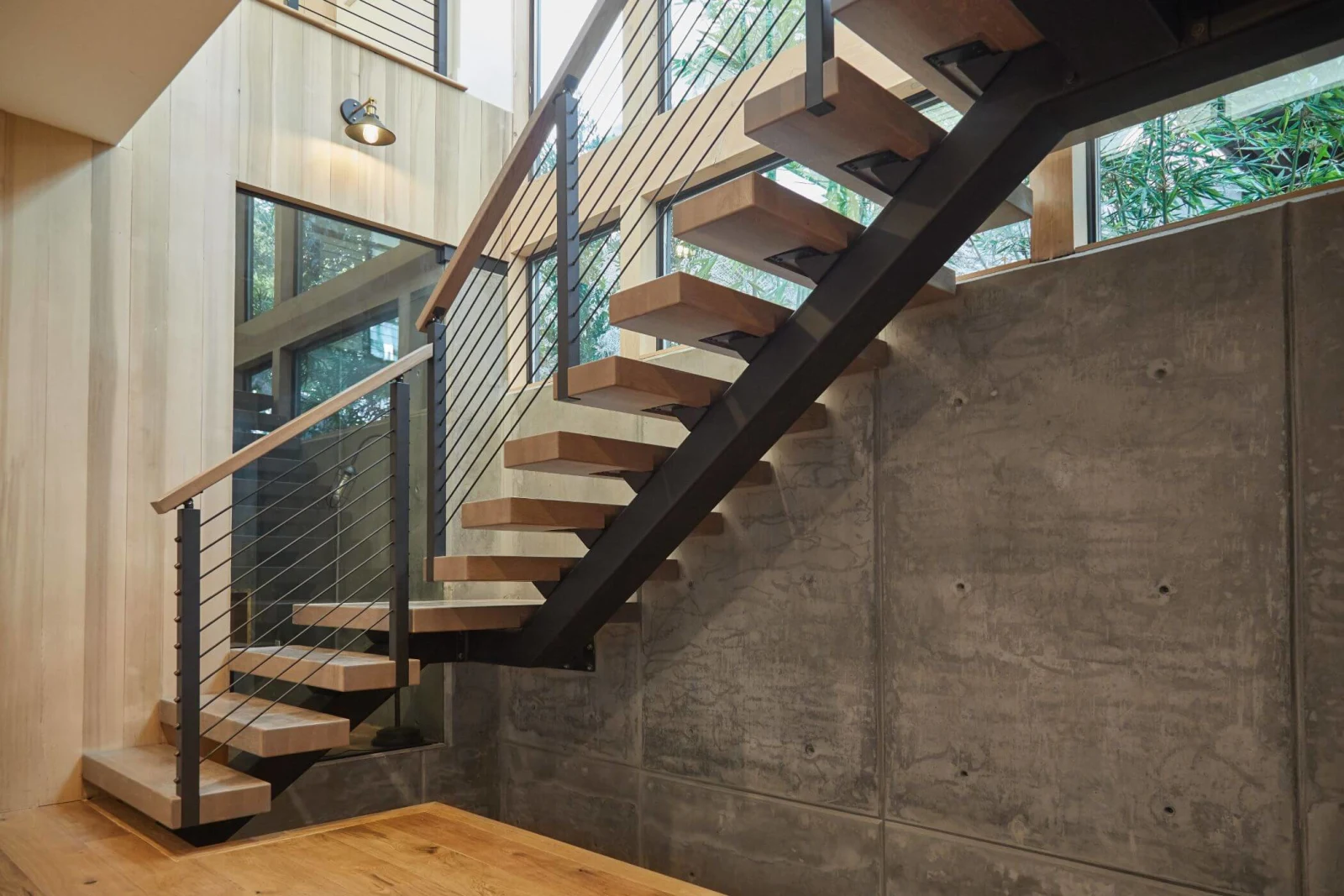 Floating stair on a black stringer set against a board-formed concrete wall