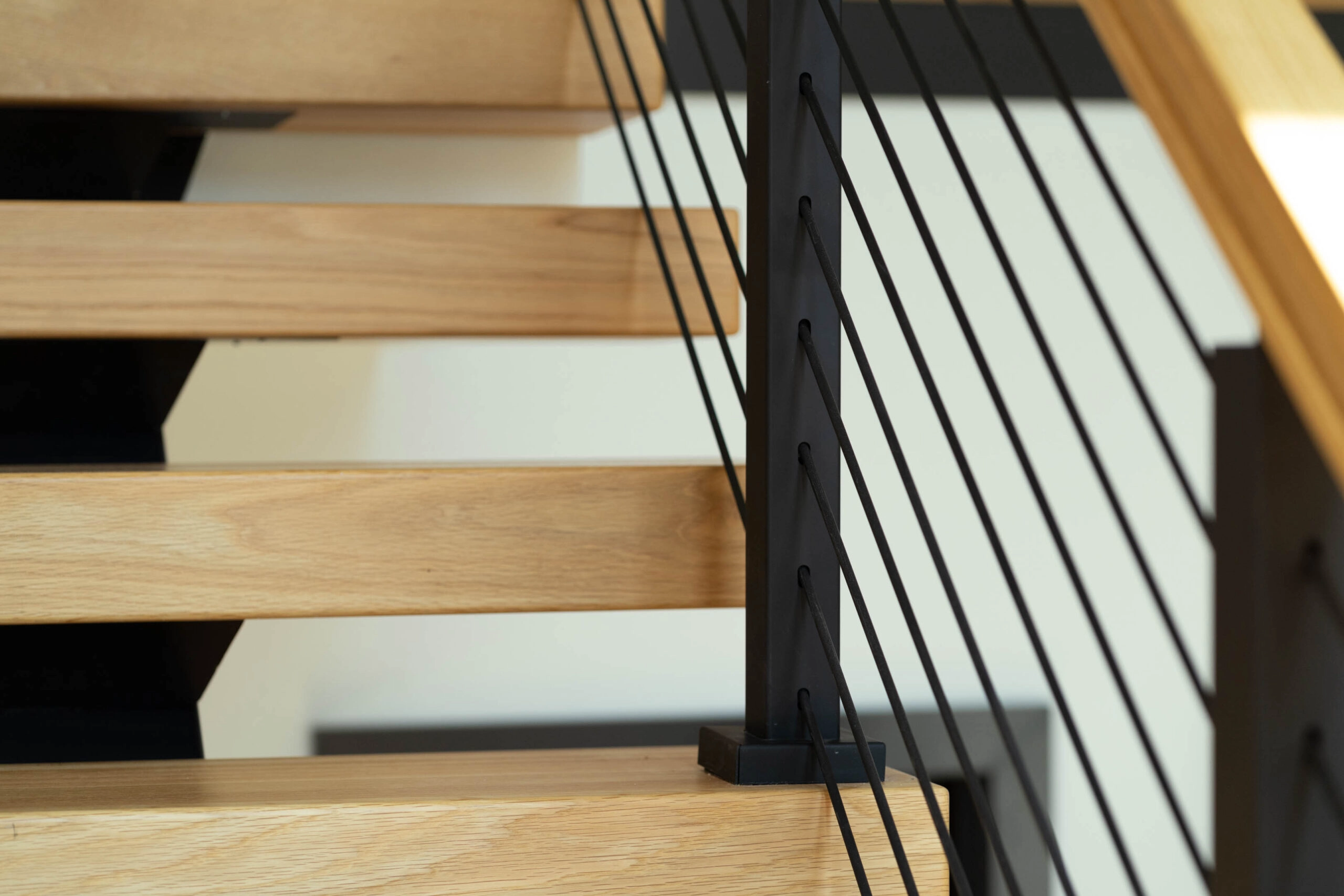 A closeup of Onyx rod cable railing mounted to the top of the treads on a FLIGHT Mono floating staircase with light wood treads.