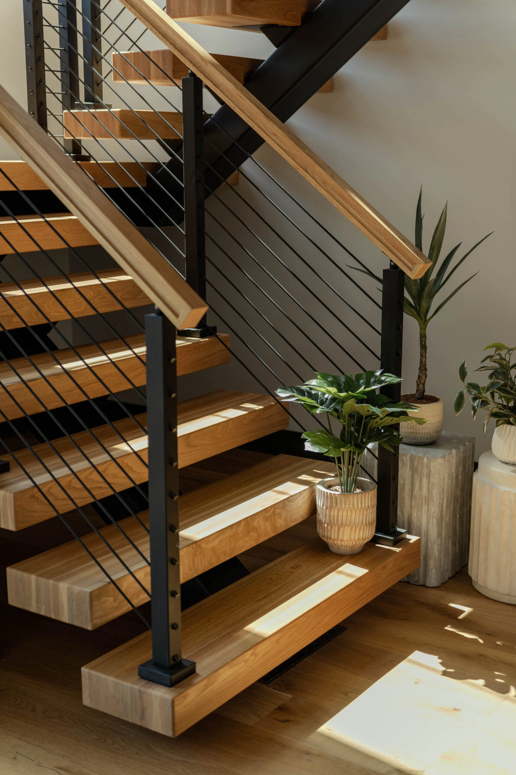 Rod infill in black posts runs beside warm-stained treads and potted plants