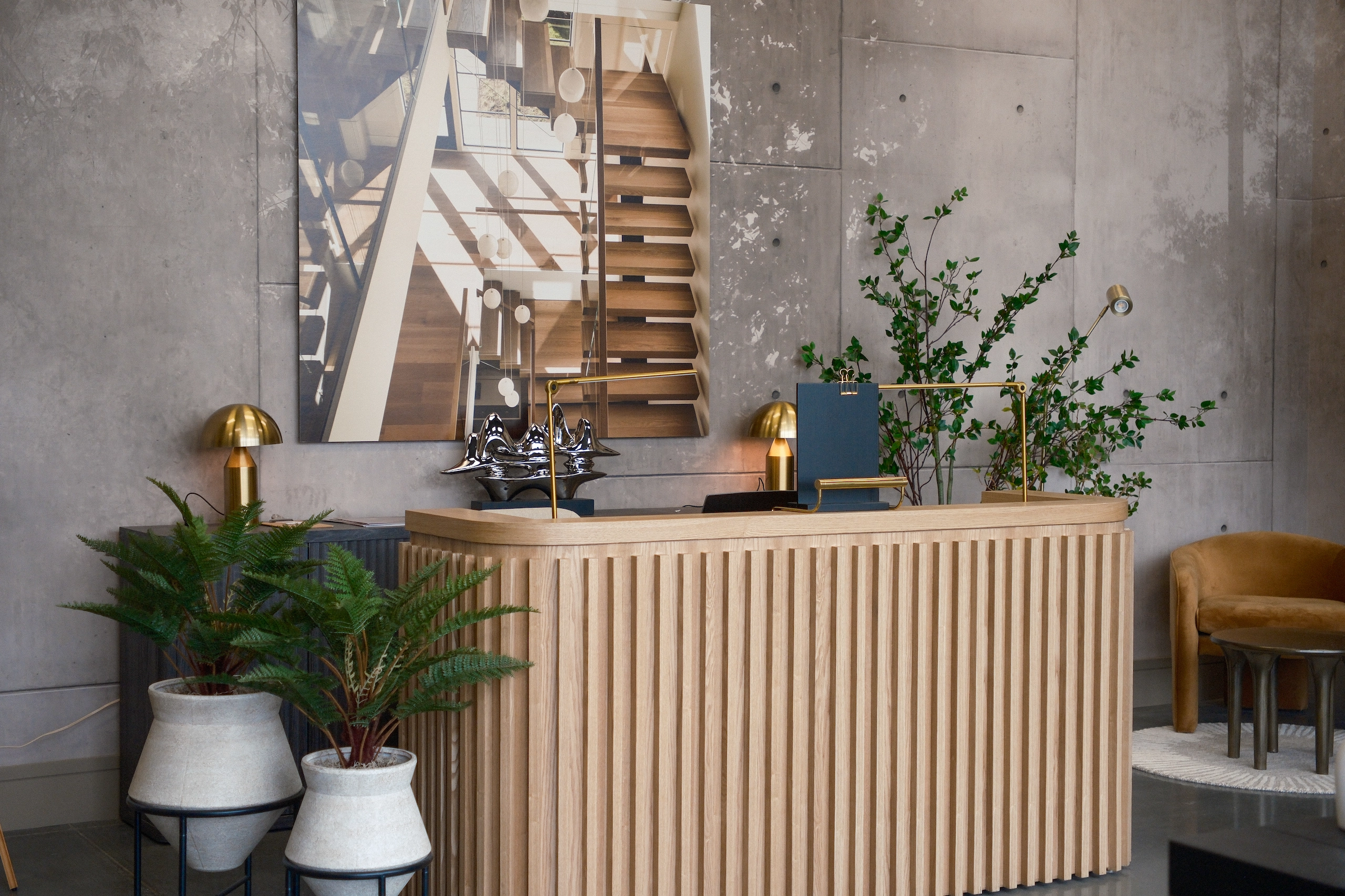 A fluted reception desk stands before a spiral stair display and greenery