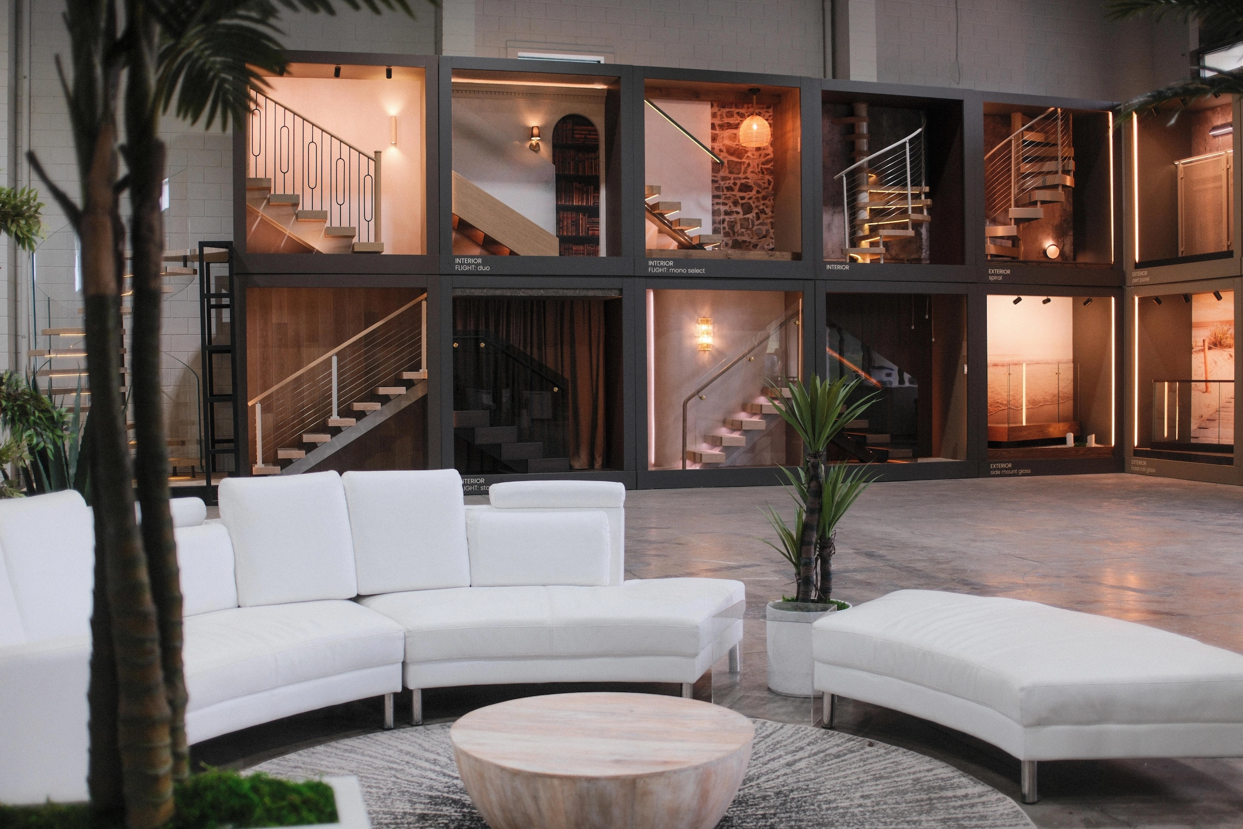 White seating and a palm sit before a wall of lit stair display bays