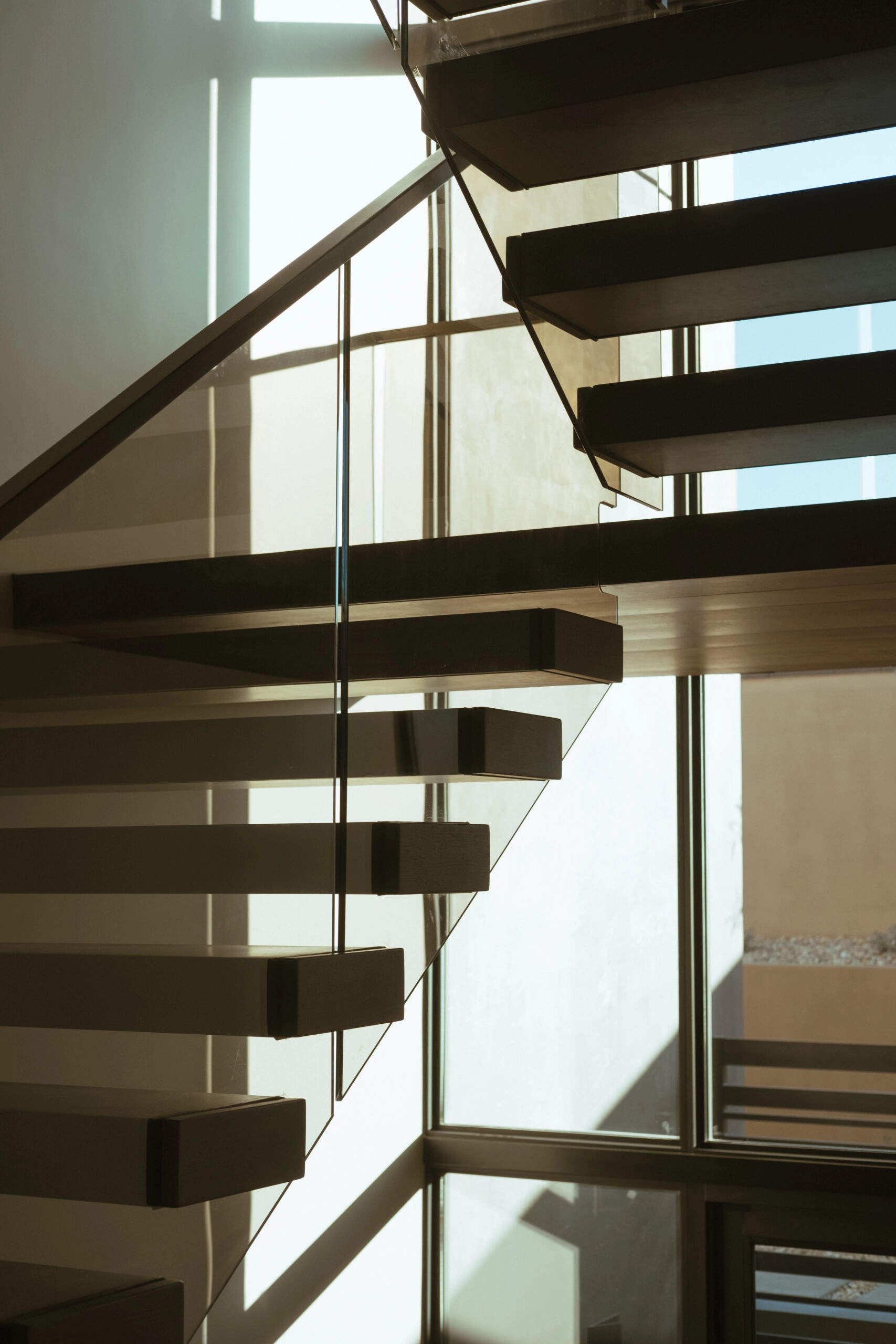 A switchback cantilever stair crosses a sunlit window wall behind glass