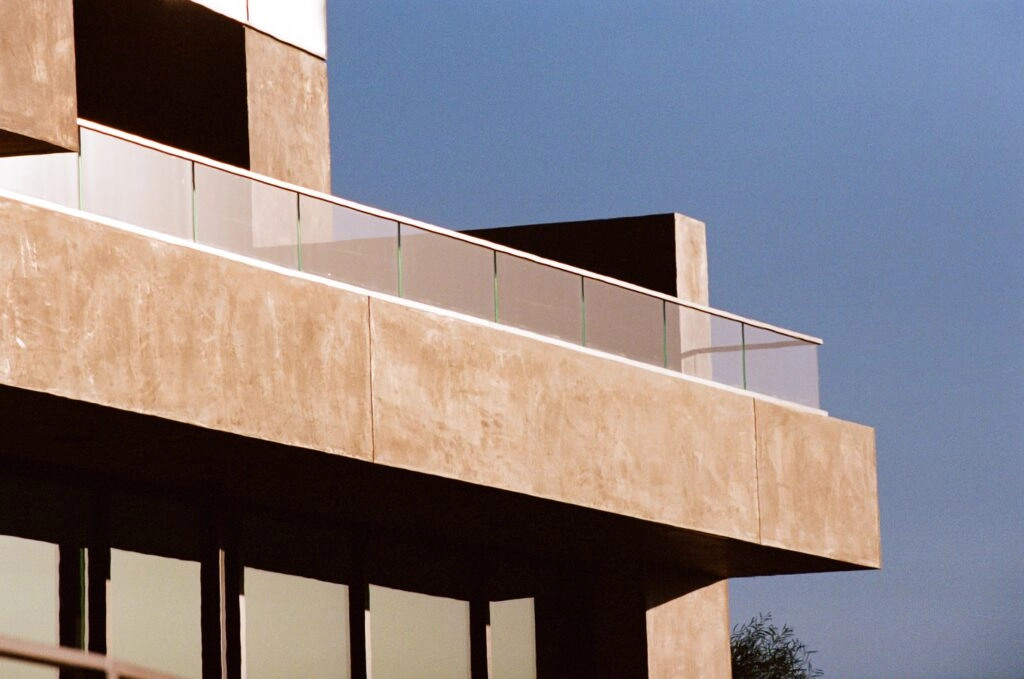 Glass railing wraps a cantilevered balcony on a board-formed concrete facade