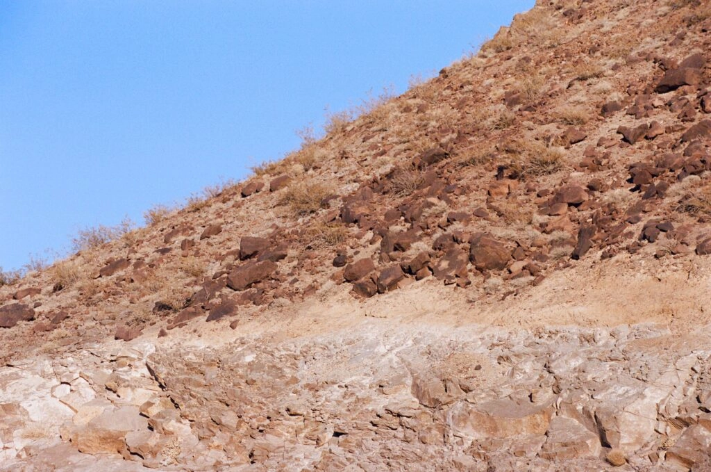 A bare rock hillside rises steeply against a clear pale desert sky