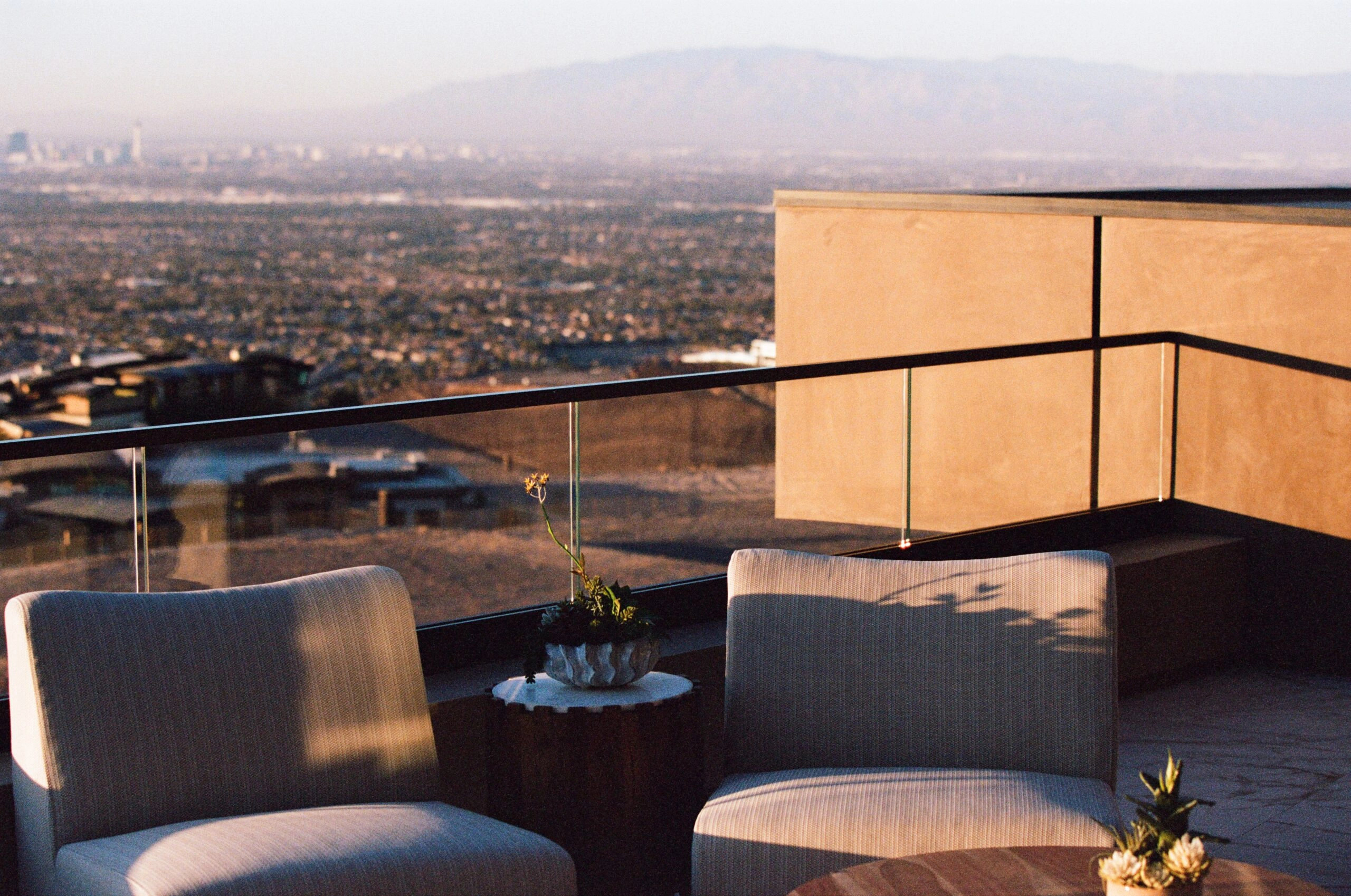 Glass railing edges a rooftop terrace above a city and distant ranges