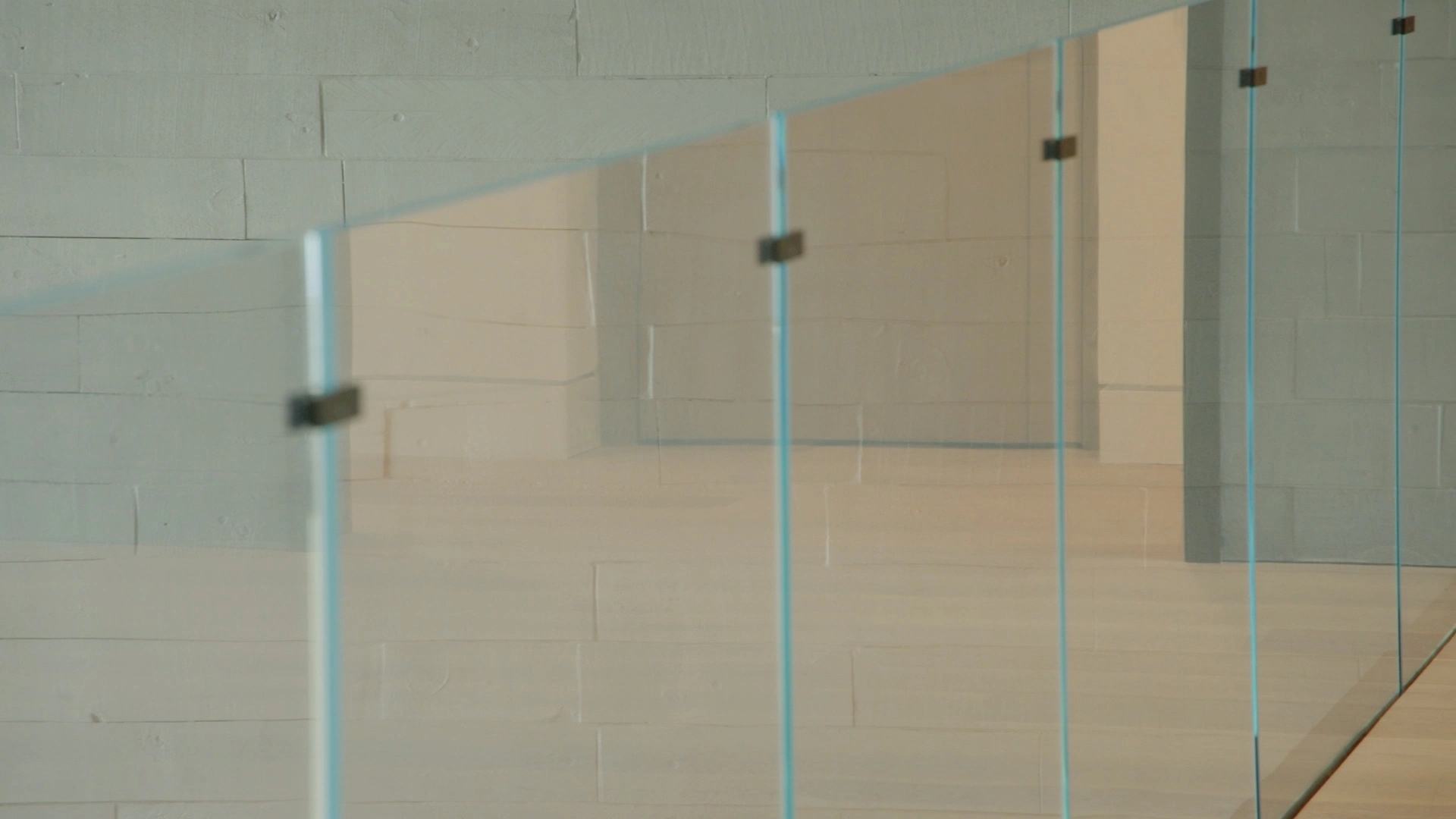 Glass panels on low black clamps edge a walkway beside a block wall