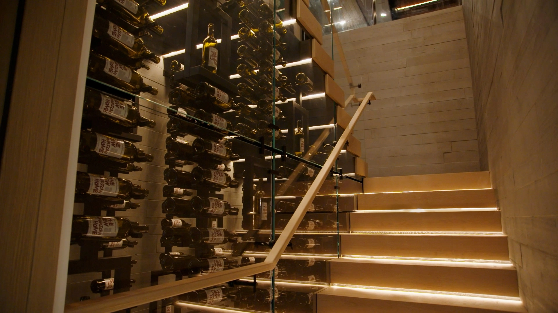 Lit treads descend past a glass-fronted wine cellar stacked with bottles