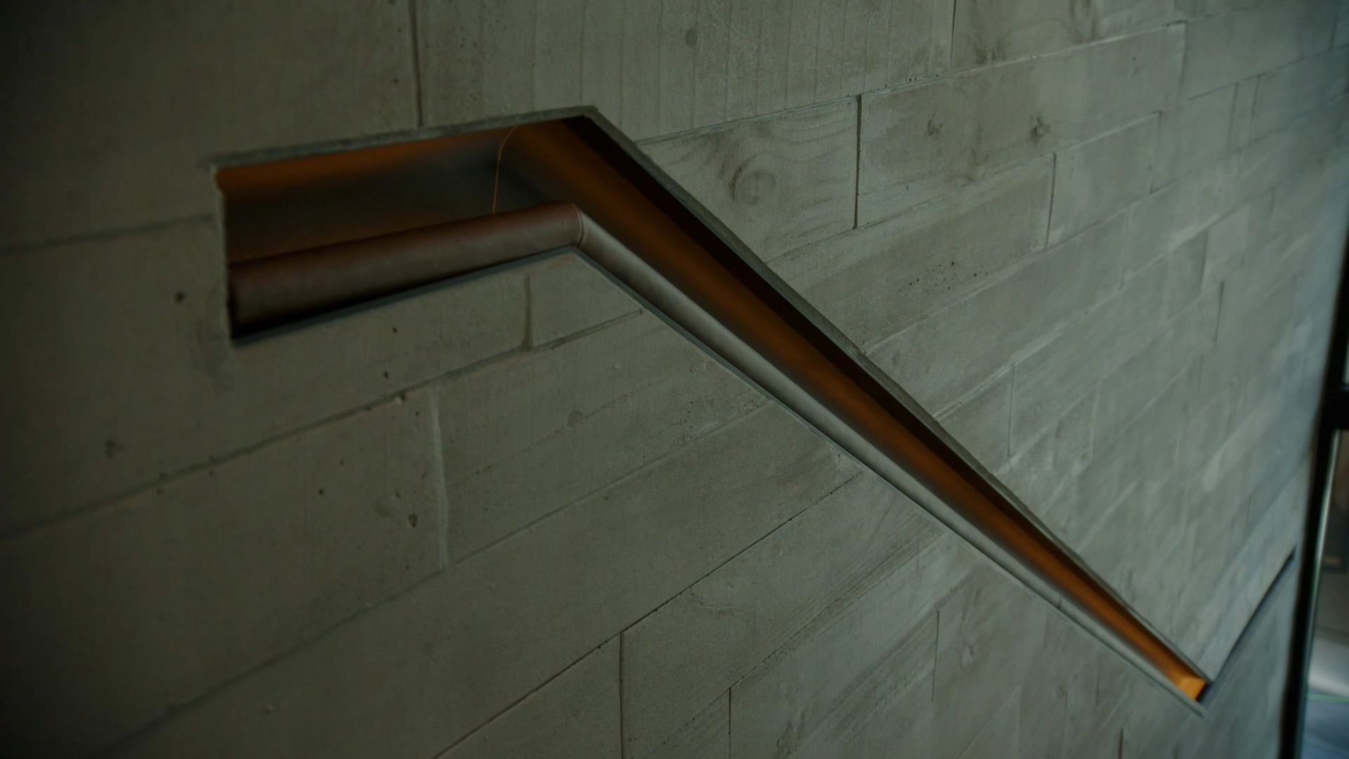 A slim wood handrail bends across a board-formed concrete wall