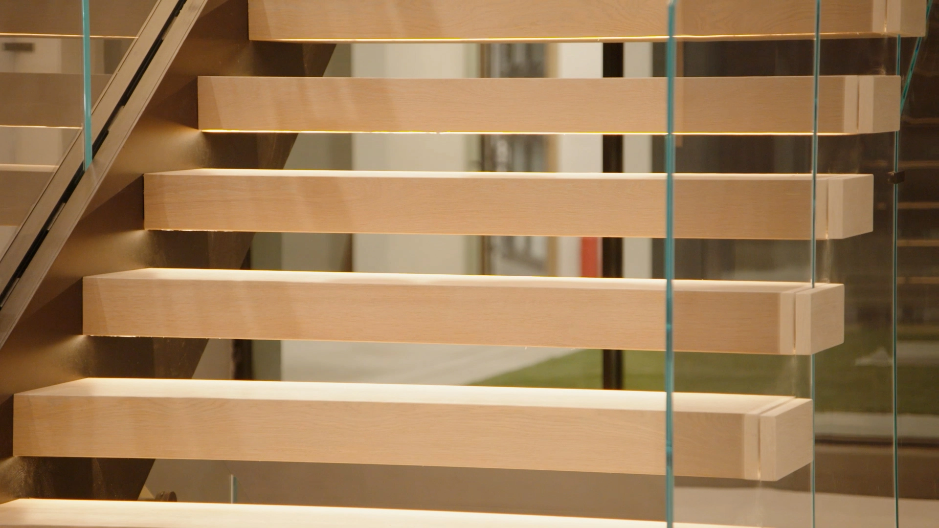 Pale treads and glass panels catch the light in a narrow stairwell