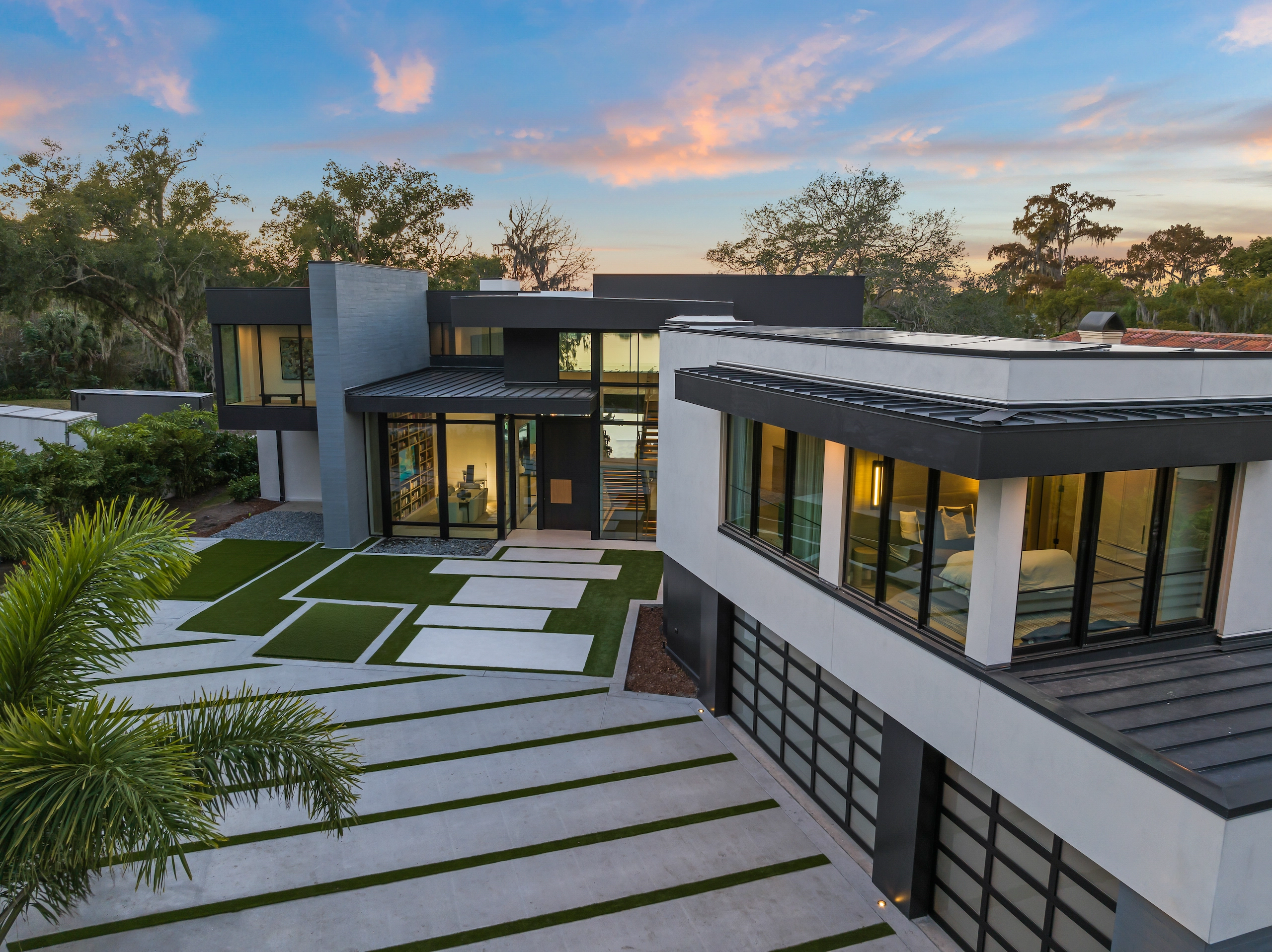 A low white home at dusk sits behind a banded concrete and grass walk