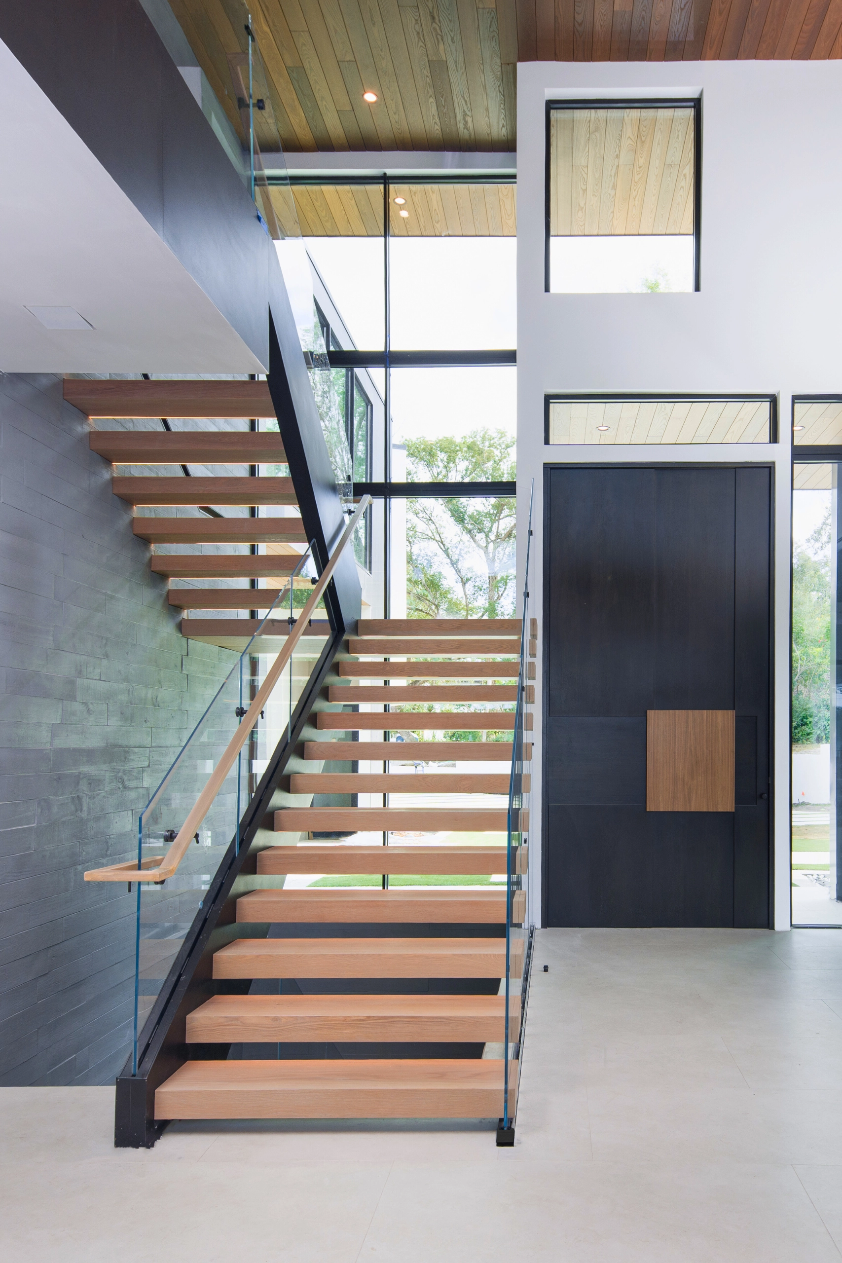 A floating stair on a black stringer climbs beside a glazed entry corridor