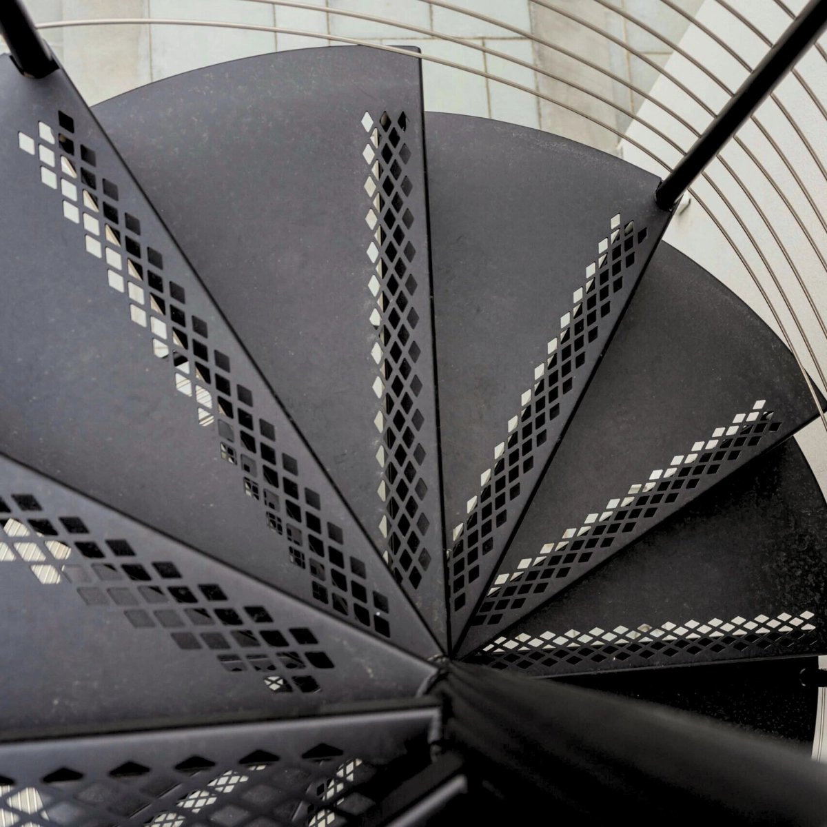 Perforated black treads fan out around the column of a spiral stair
