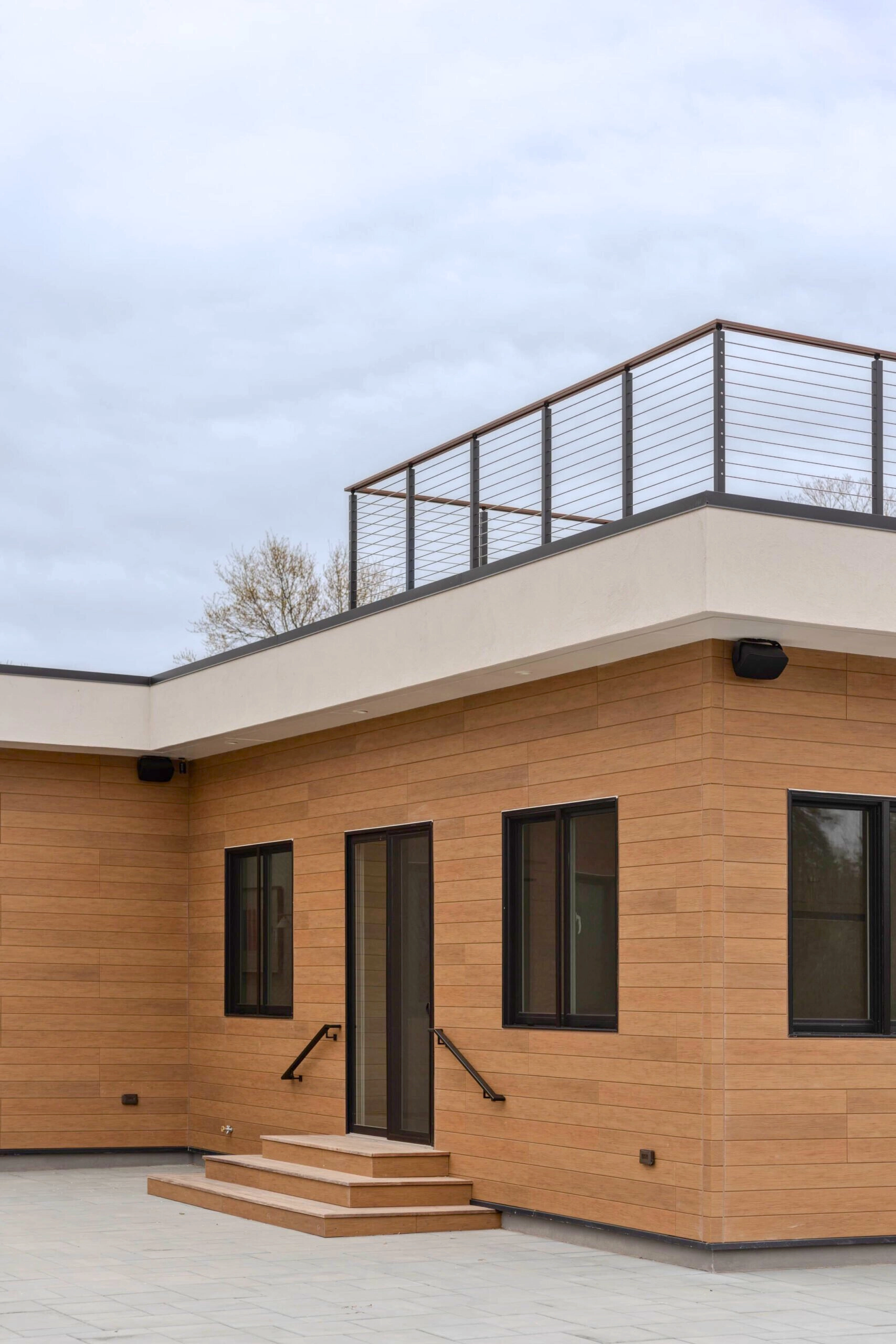 Cable railing outlines a roof deck above a wood and stucco exterior