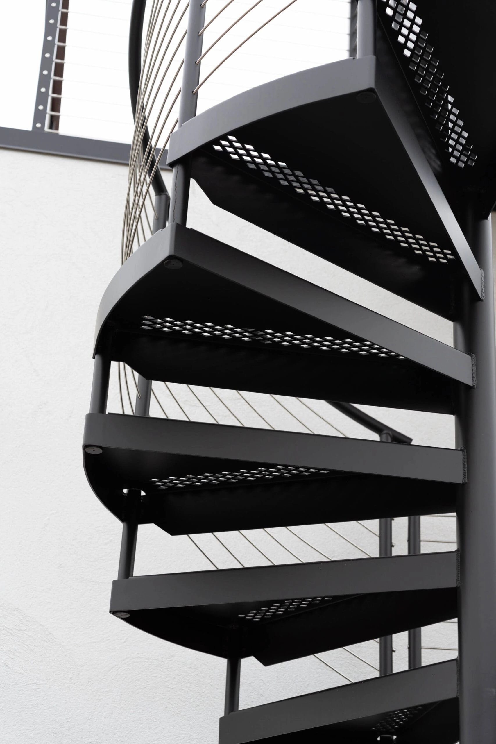 The spiral stair's perforated treads wind past a bright white wall