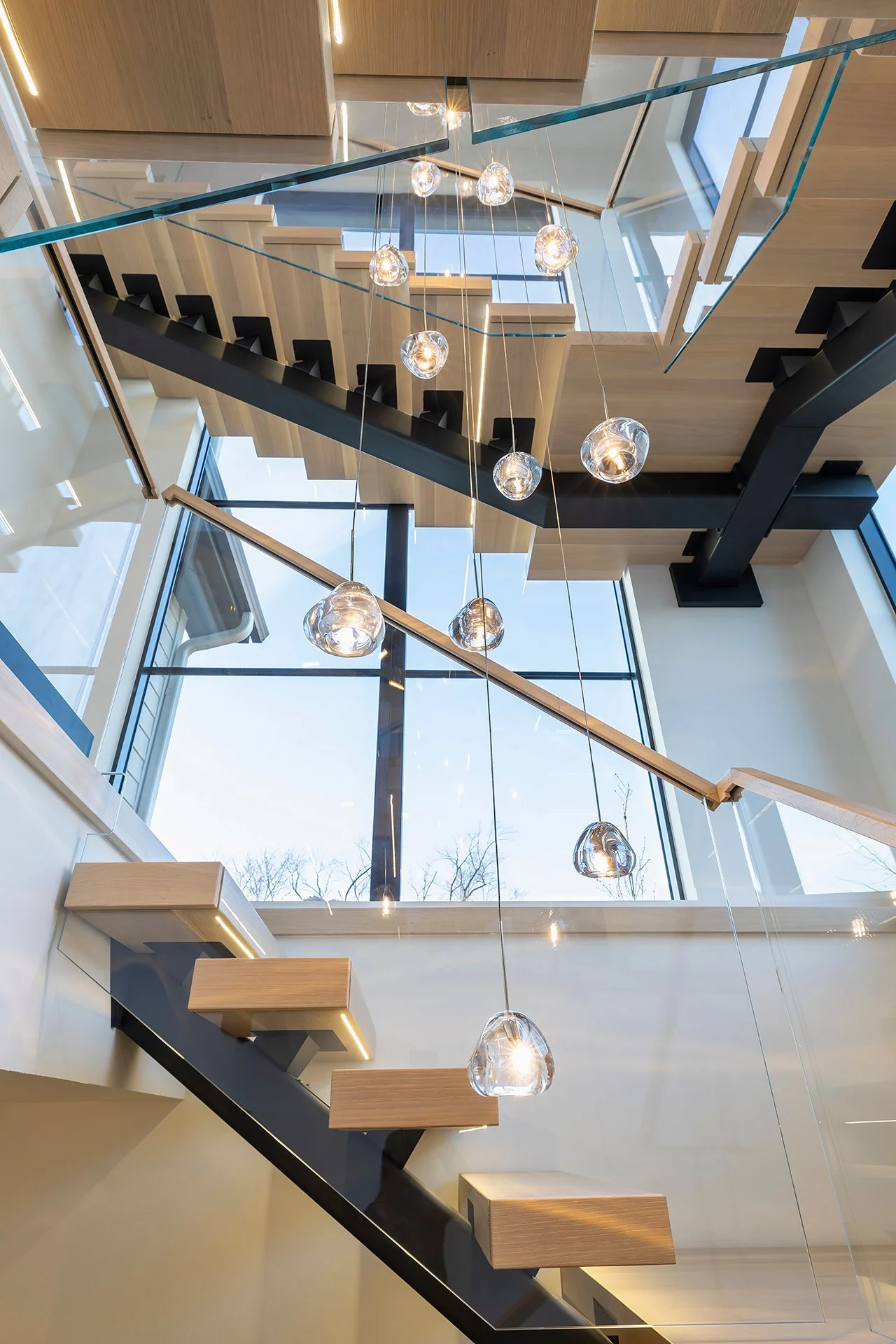 Floating treads and pendant globes crowd the view up a bright stairwell