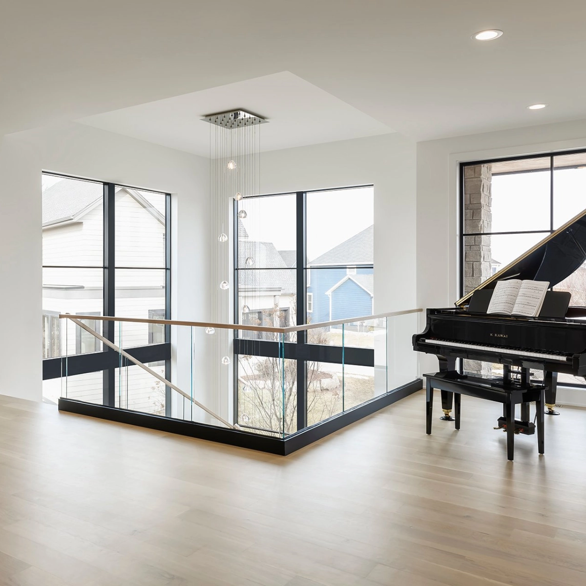 Glass railing rings a stairwell opening in a room with a grand piano