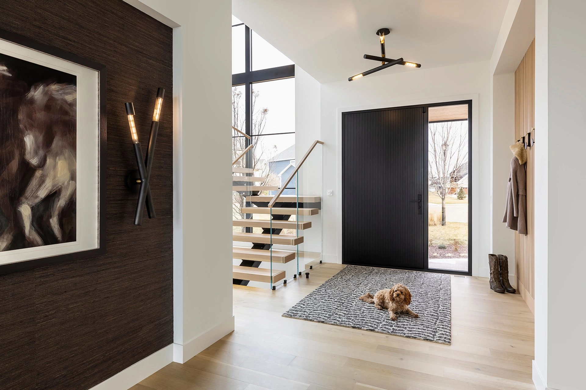 A floating stair with glass railing rises at the end of a bright entry hall