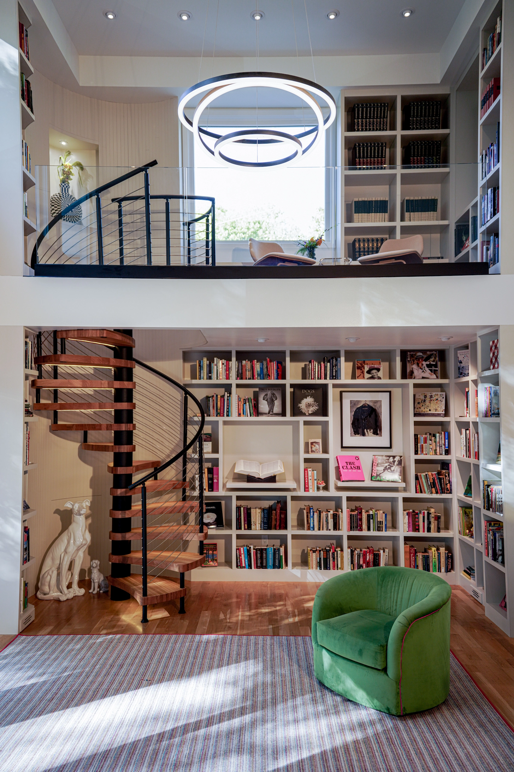 The spiral stair links a book-lined room to the landing under a round window