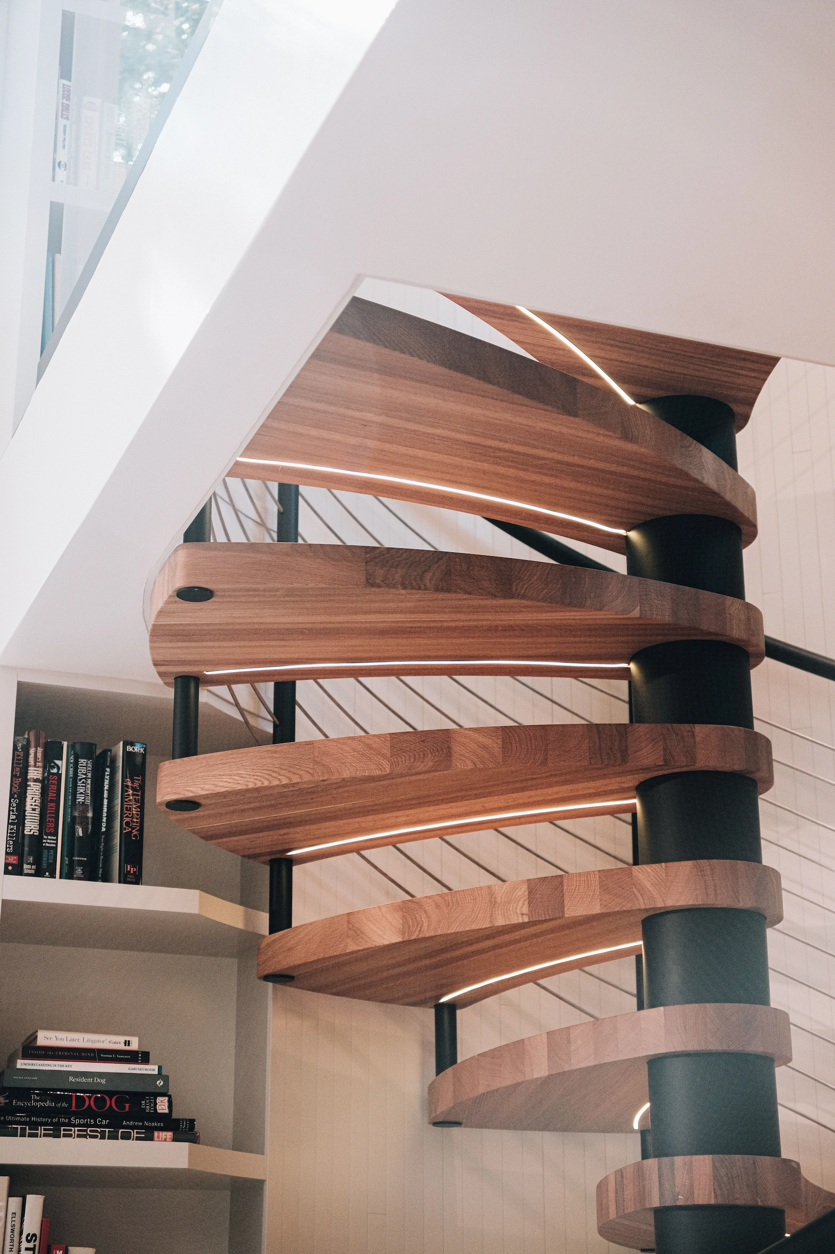 Wood treads spiral overhead around a black column above a wall of books