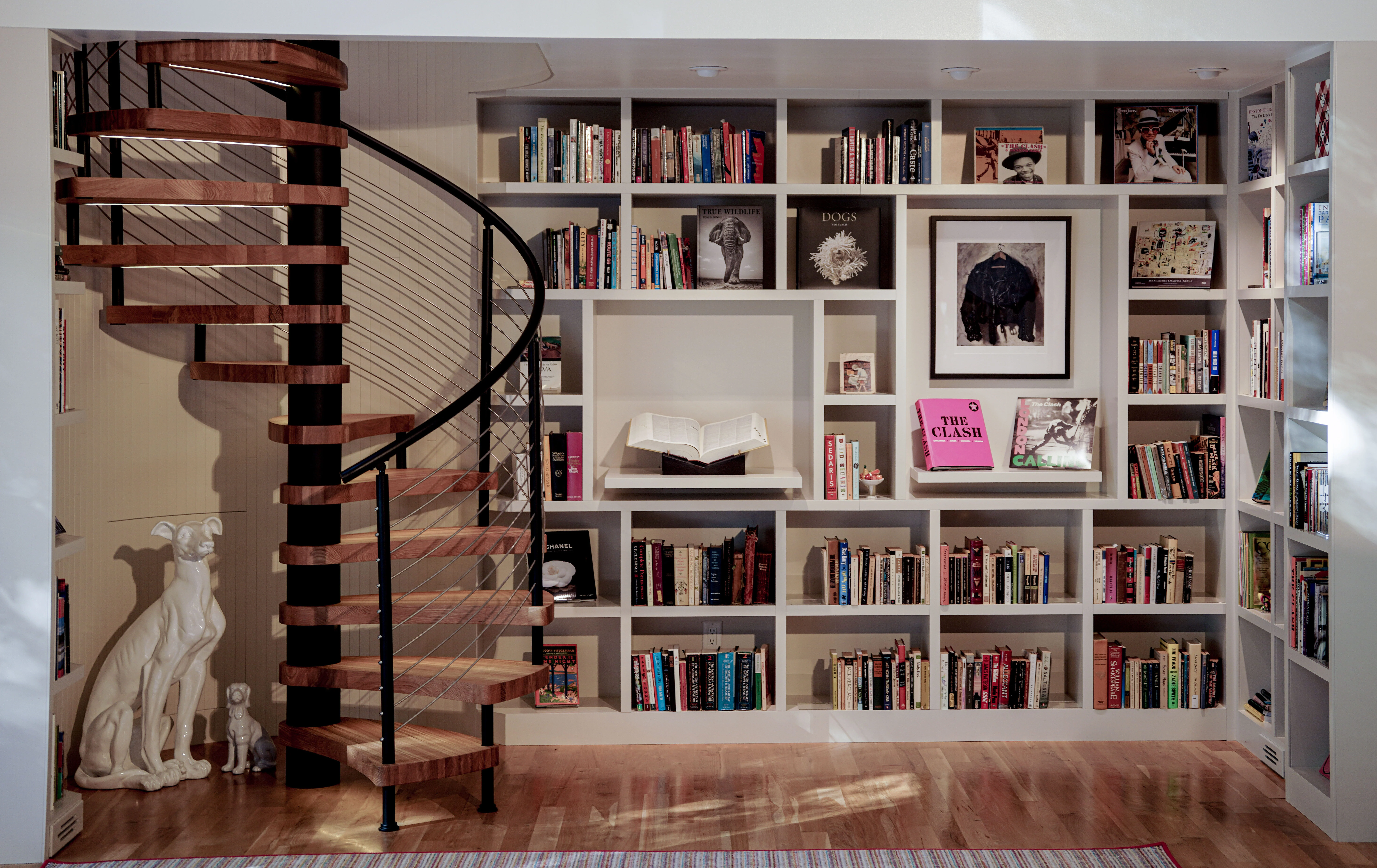 A spiral stair turns beside floor-to-ceiling shelves in a picture-hung library