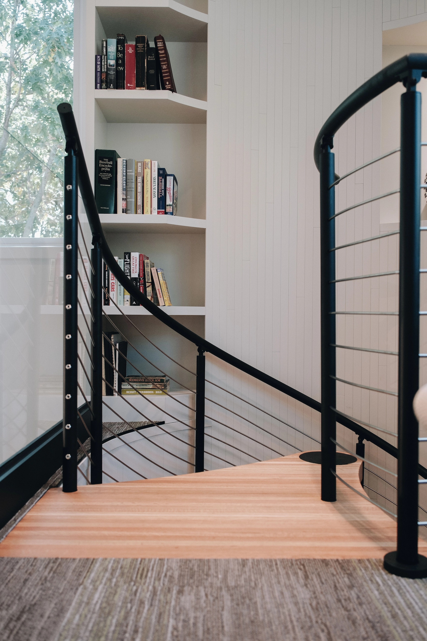 Rod infill curves with a spiral stair's railing beside built-in bookshelves