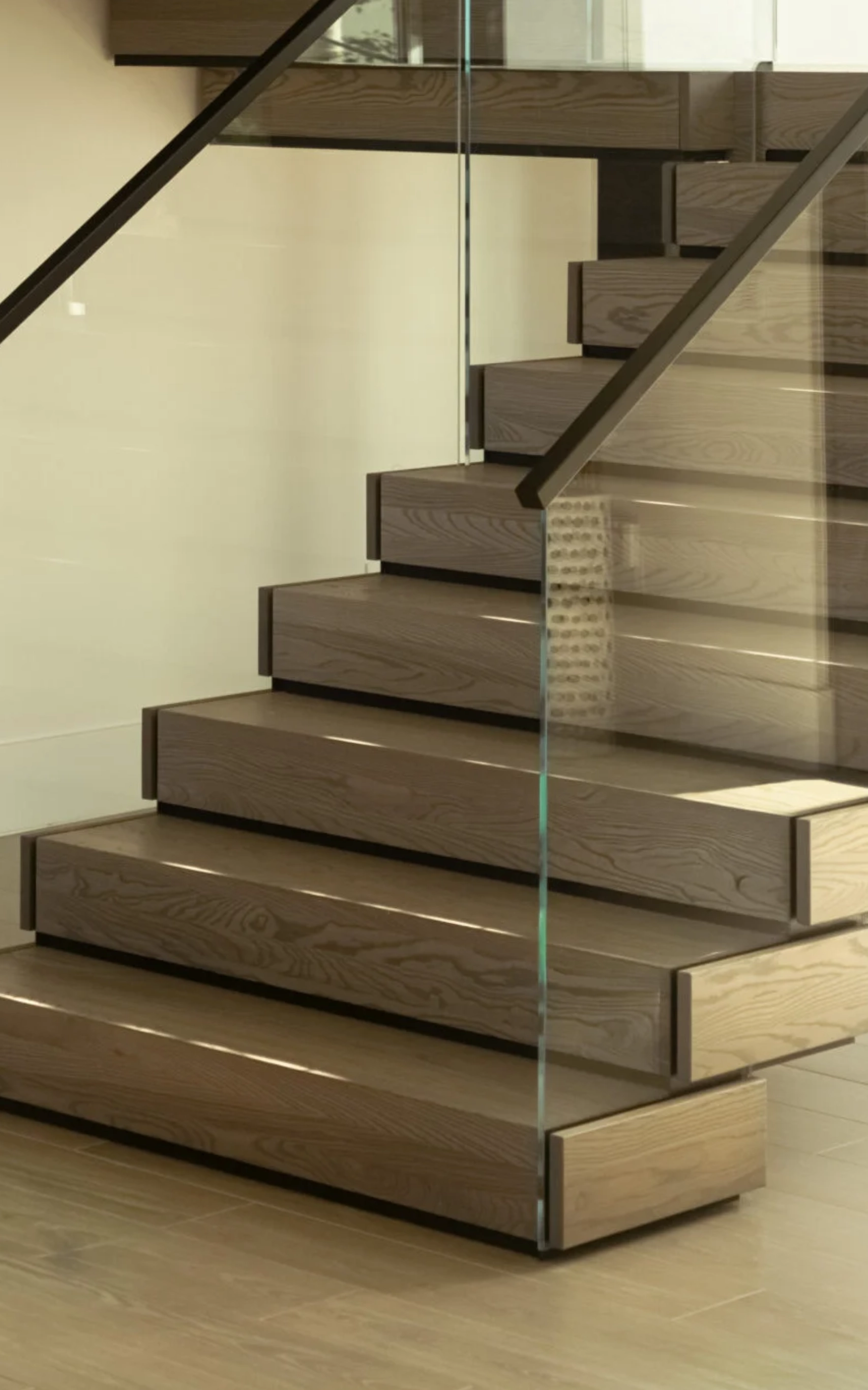 Stacked treads and a glass panel meet the floor at the base of a stair
