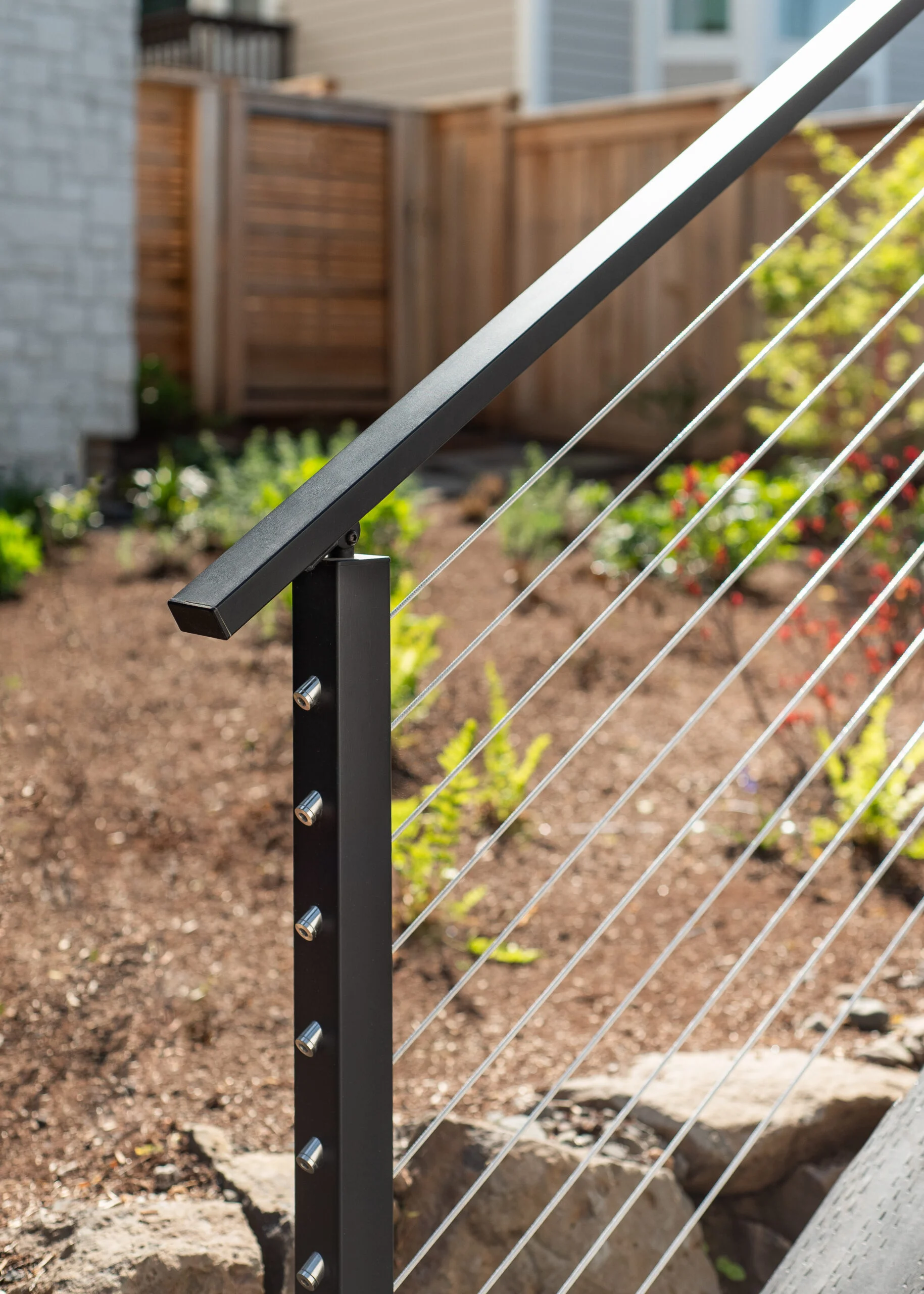 A black handrail angles down a garden stair above cable infill