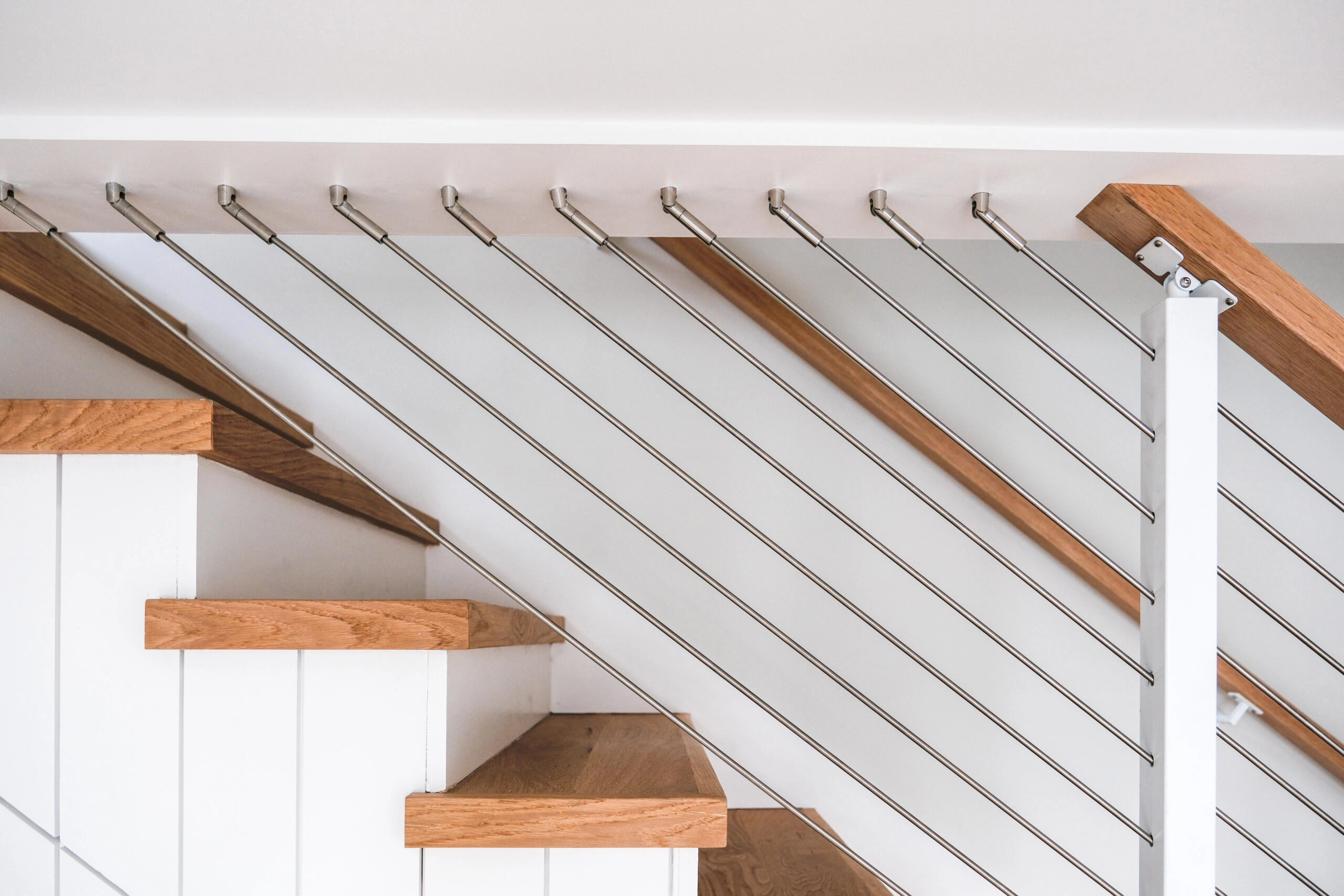 Rod infill spans white posts beneath a sloped ceiling on an interior stair