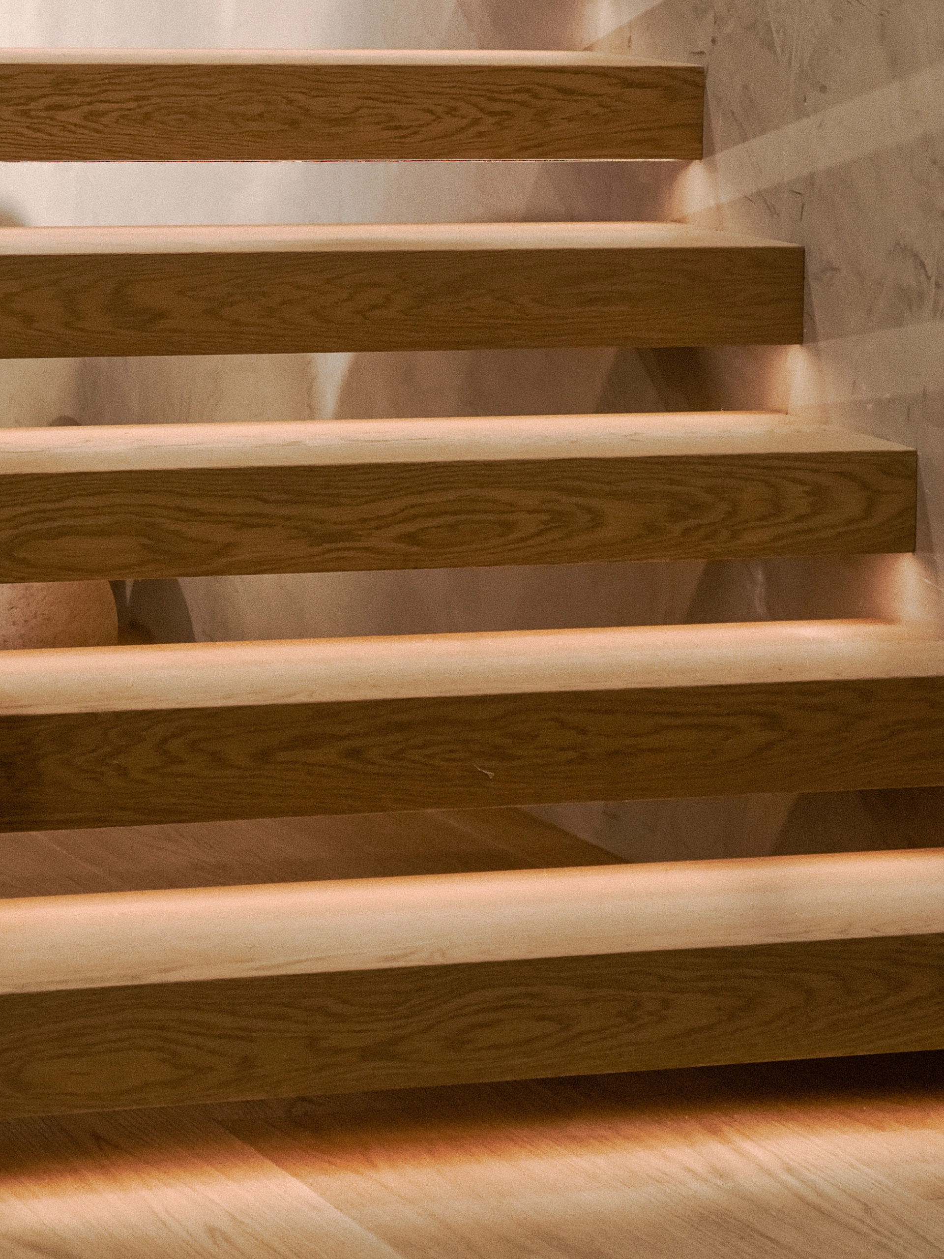 A strip of light runs beneath each tread on a wall-mounted floating stair