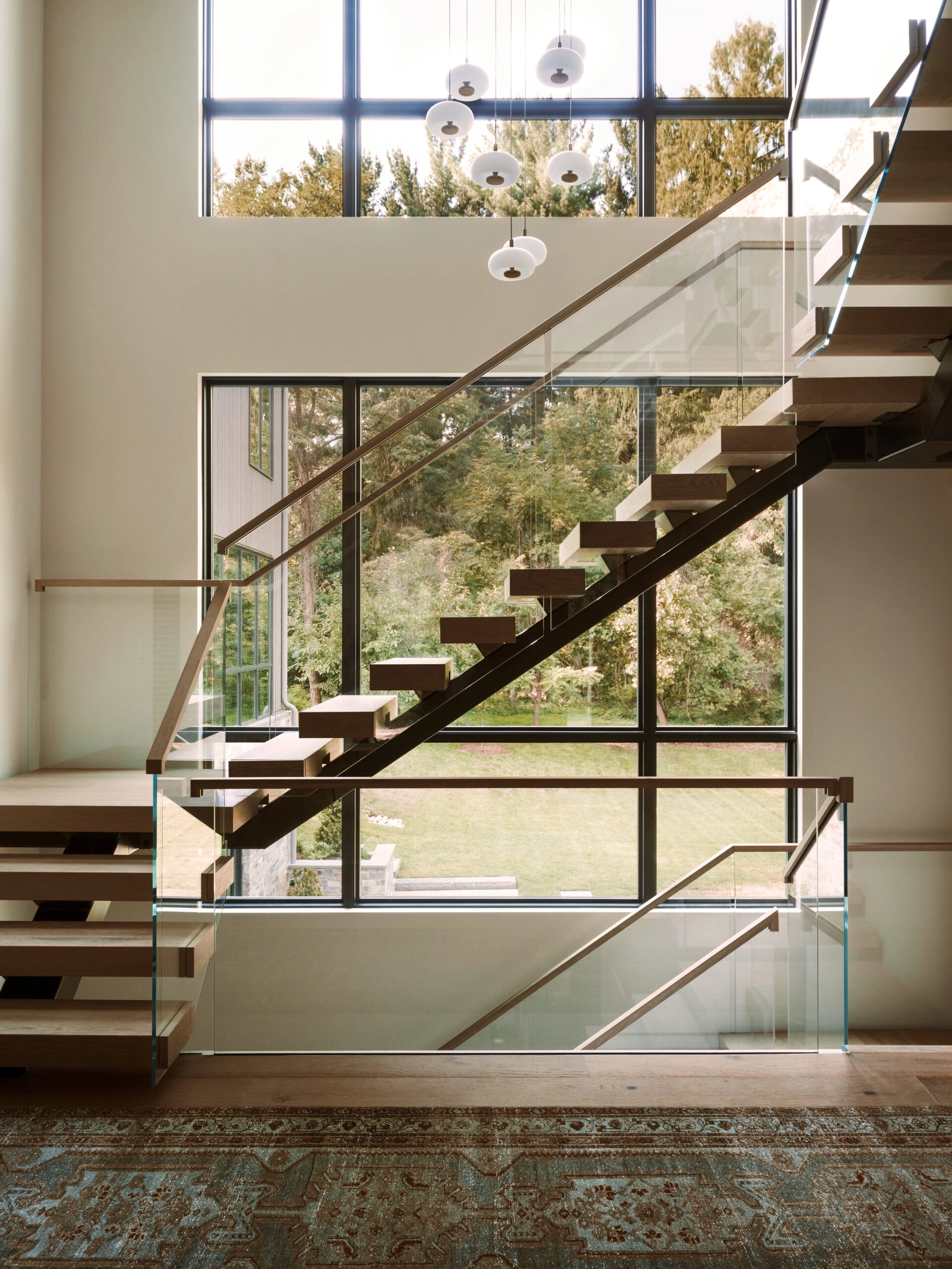 A stair with a wood-capped glass railing crosses a wall of tall windows