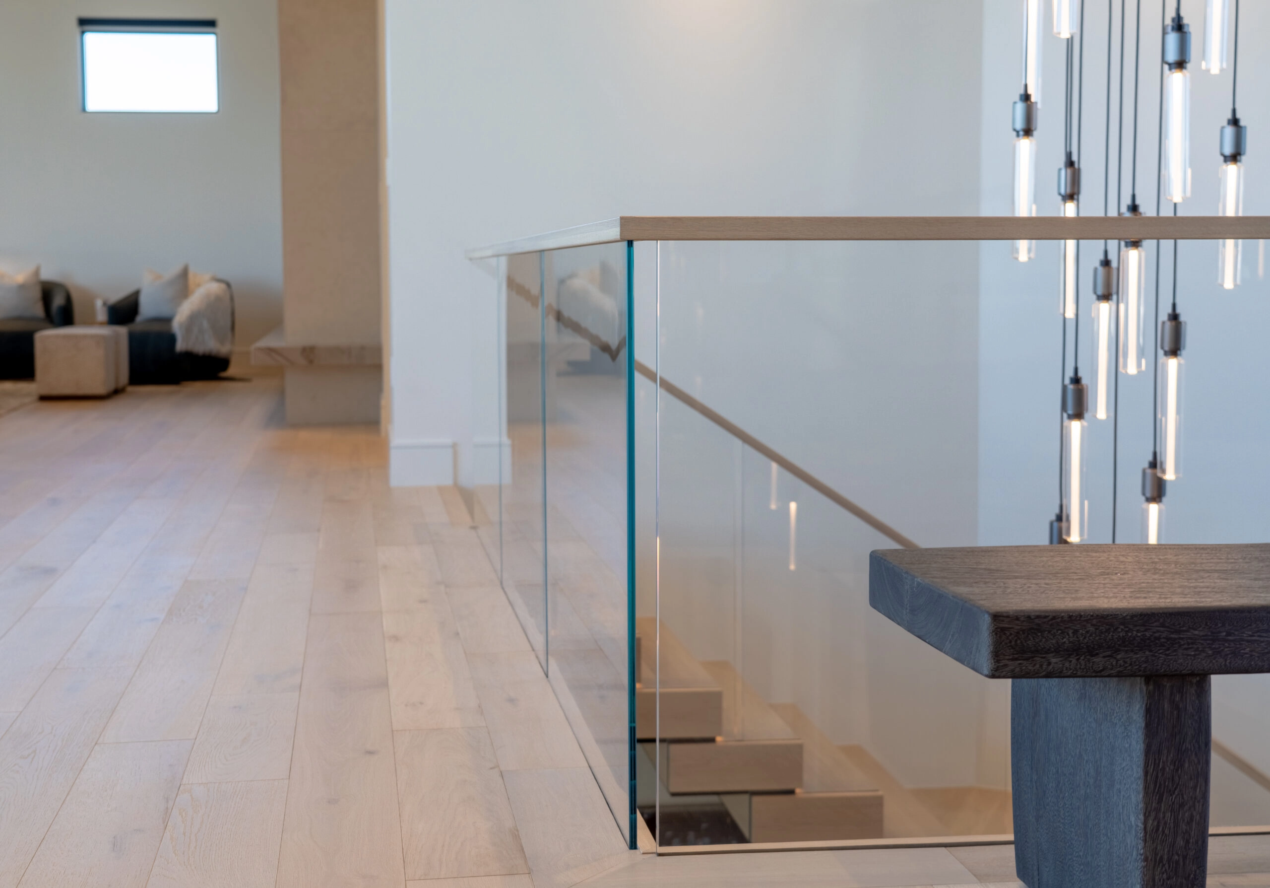 A wood-capped glass railing edges an upper floor beside hanging pendants