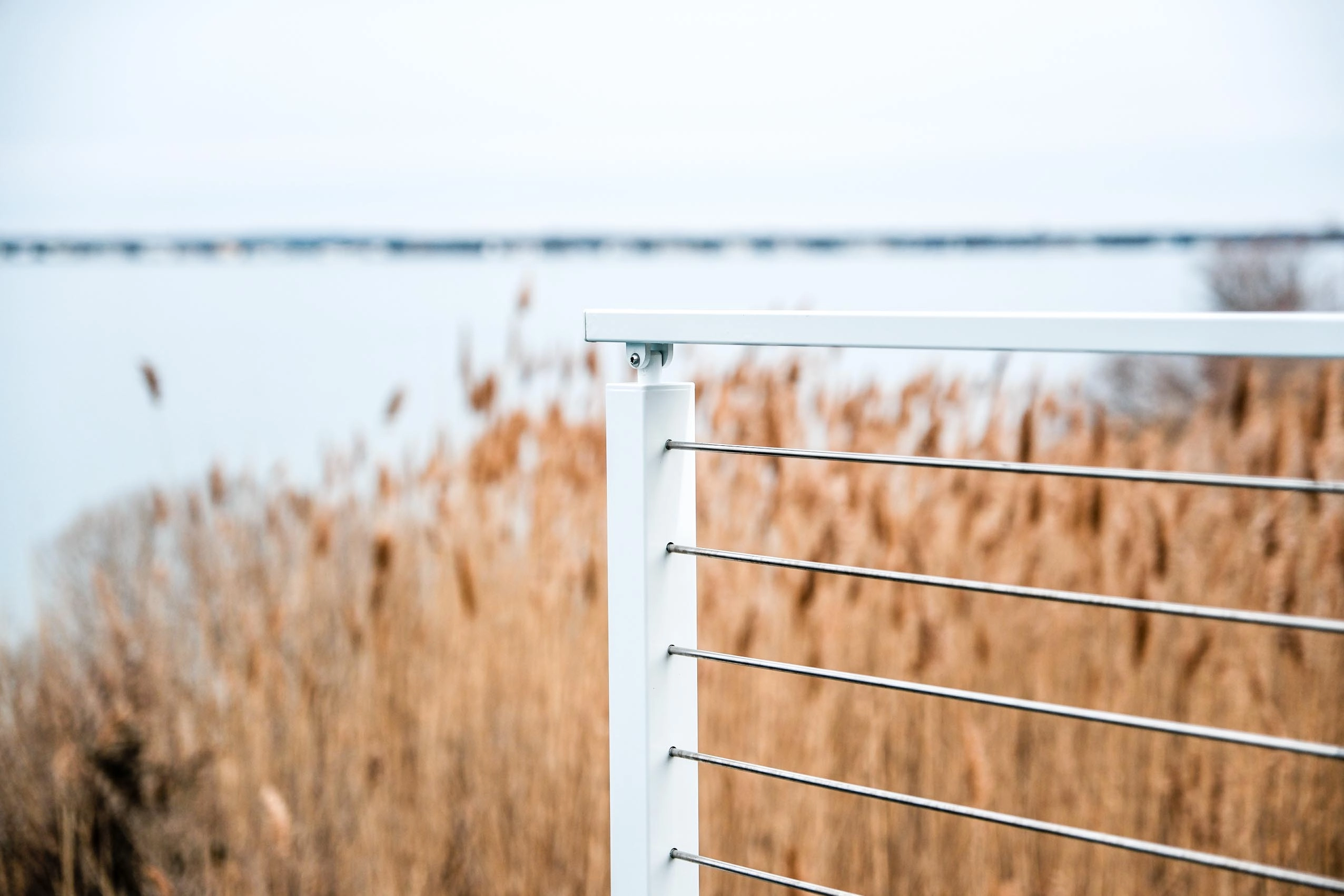Rod infill in white posts runs past beach grass toward flat open water