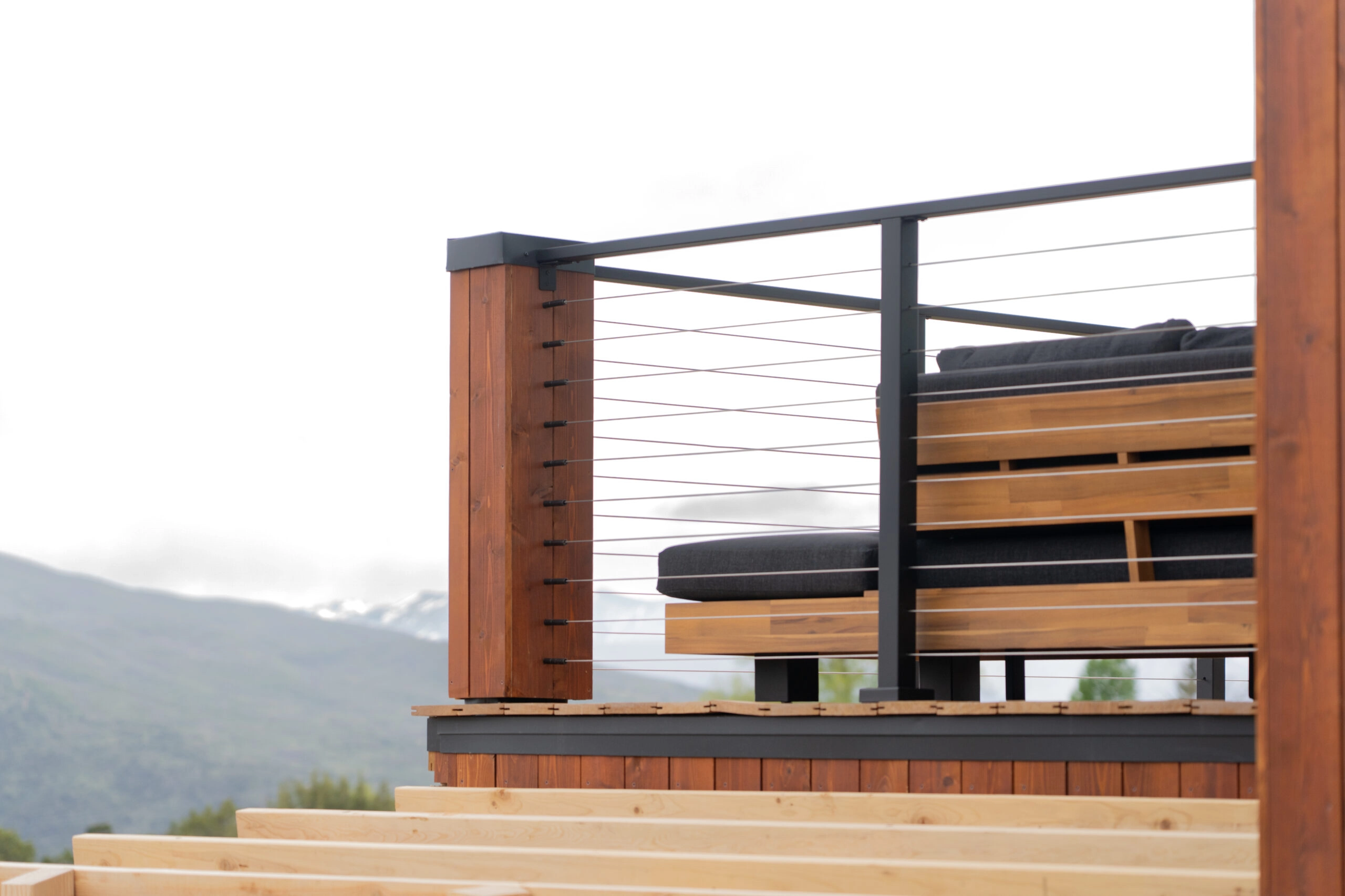 Cable railing turns a deck corner above a mountain valley, capped in black