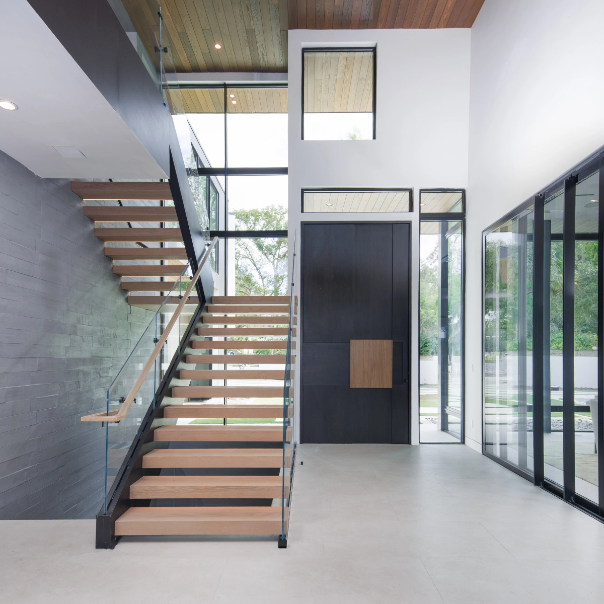Wood treads and a glass railing climb beside a tall dark entry door
