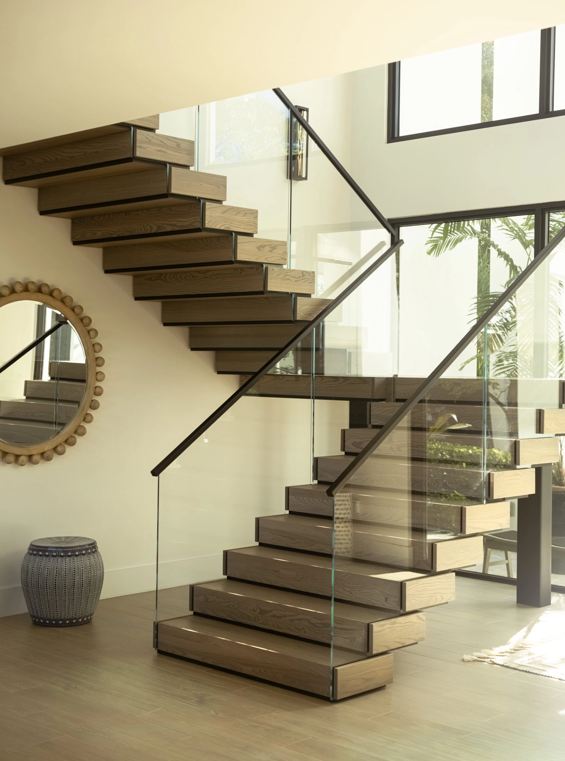 Stacked treads and a black handrail rise behind frameless glass in a bright room