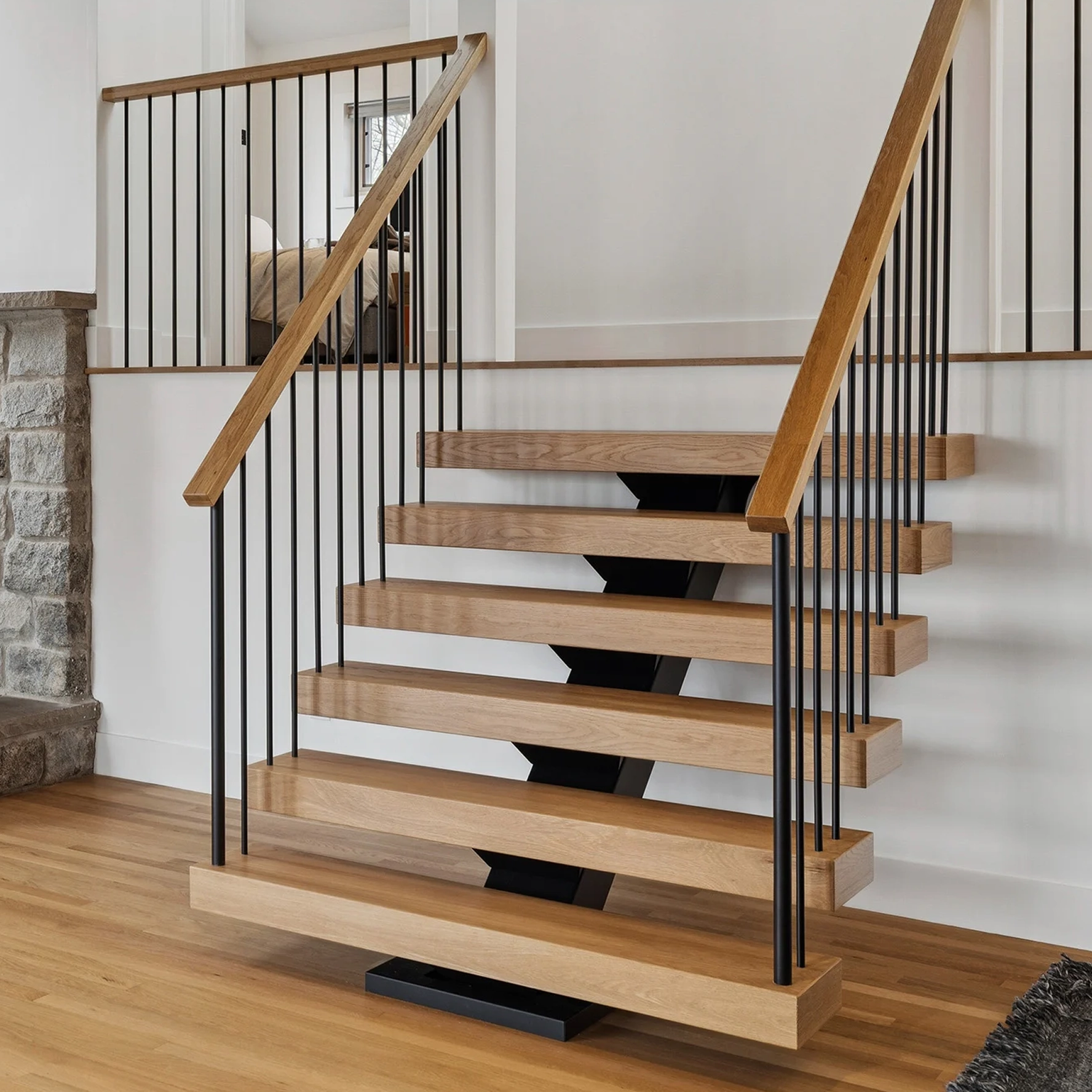 Slim black balusters and a wood handrail run alongside floating stair treads