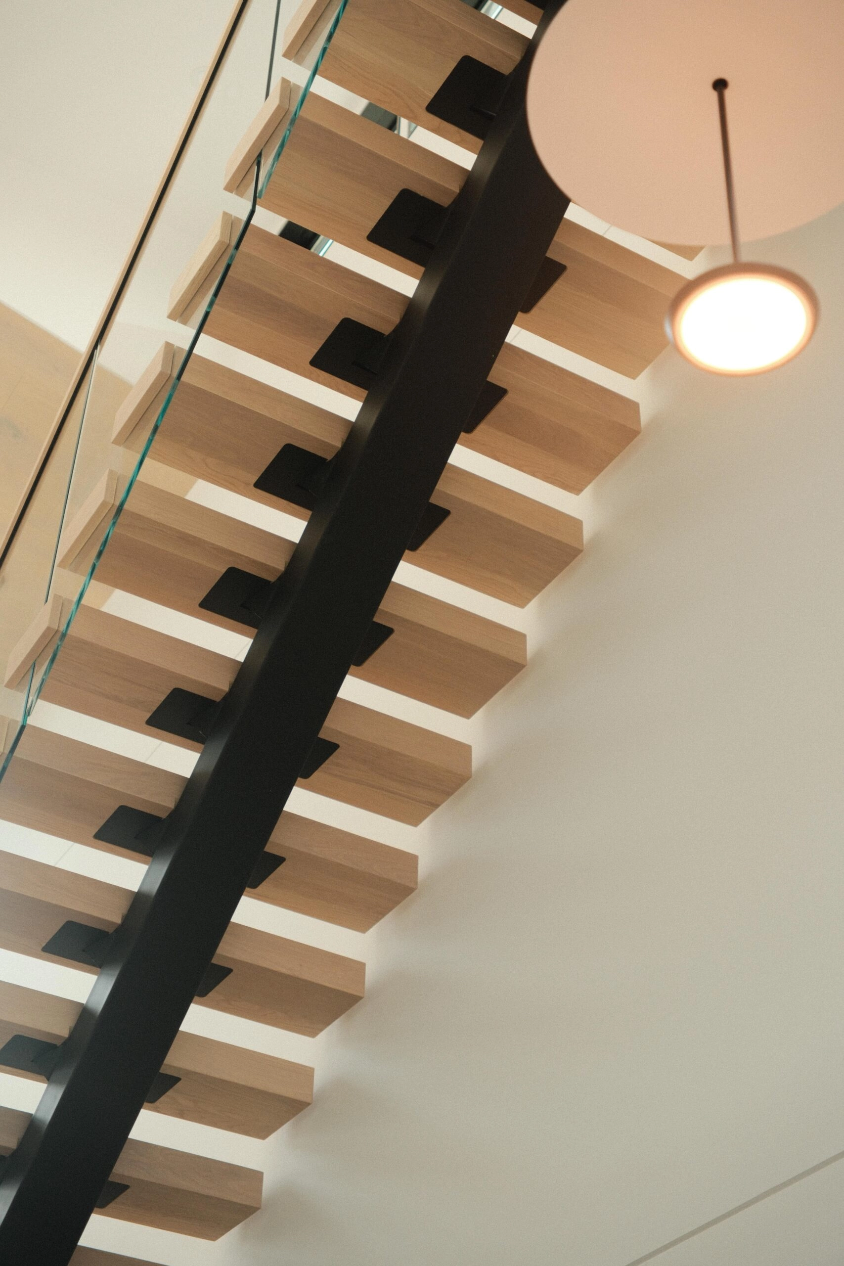 Wood treads step up a single black stringer past a hanging globe pendant