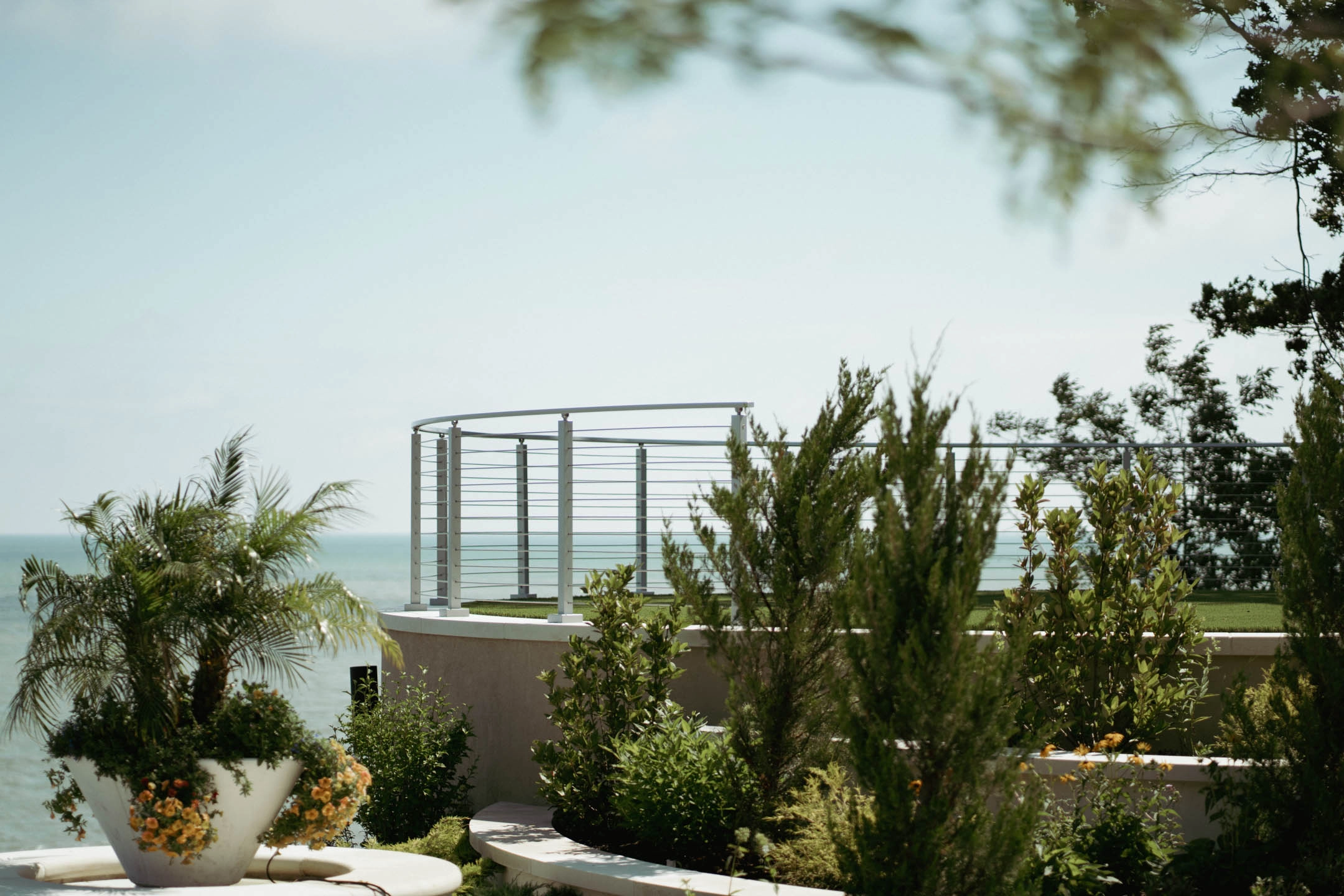 Curved rod railing follows a planted terrace high above open water