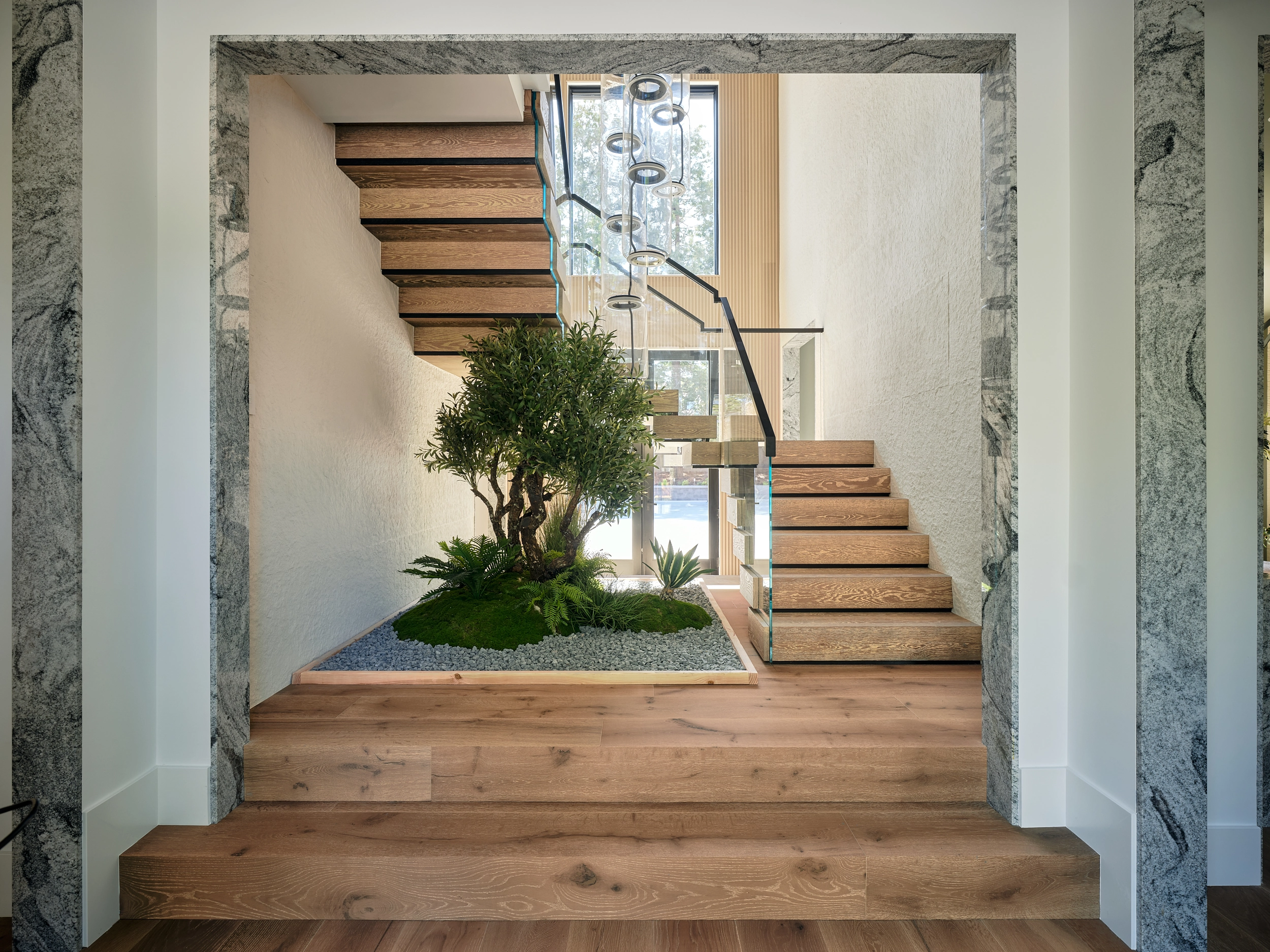 A U-turn stair with glass railing wraps an indoor tree in a stone-framed entry