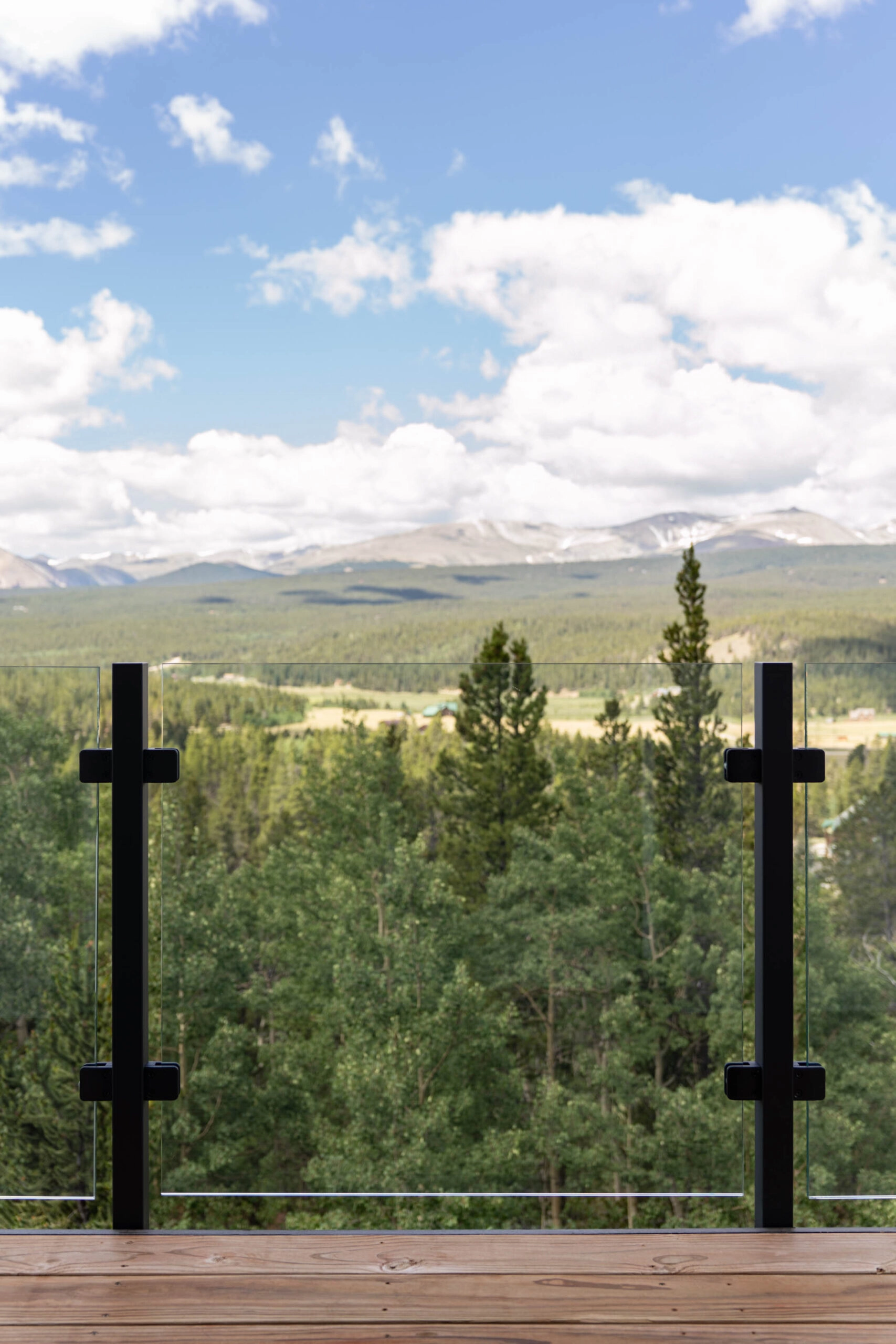 Black posts hold glass panels on a deck above pines and a mountain range