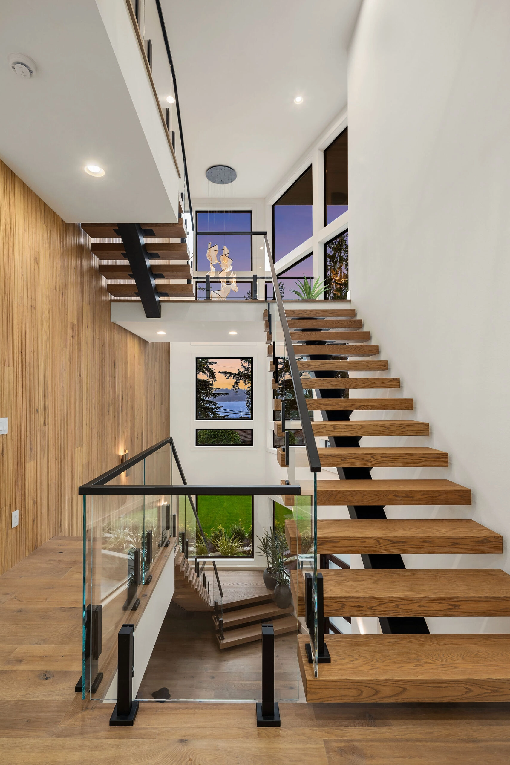 A tall stairwell pairs a center-stringer floating stair with glass panel railing
