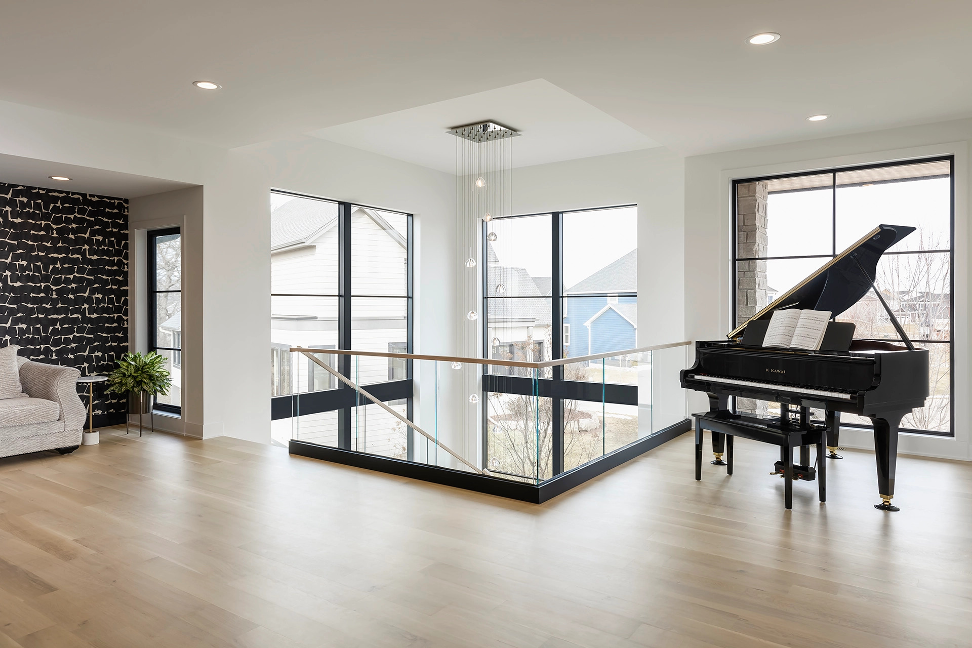 Glass railing with a black base rail edges an upper floor beside a grand piano