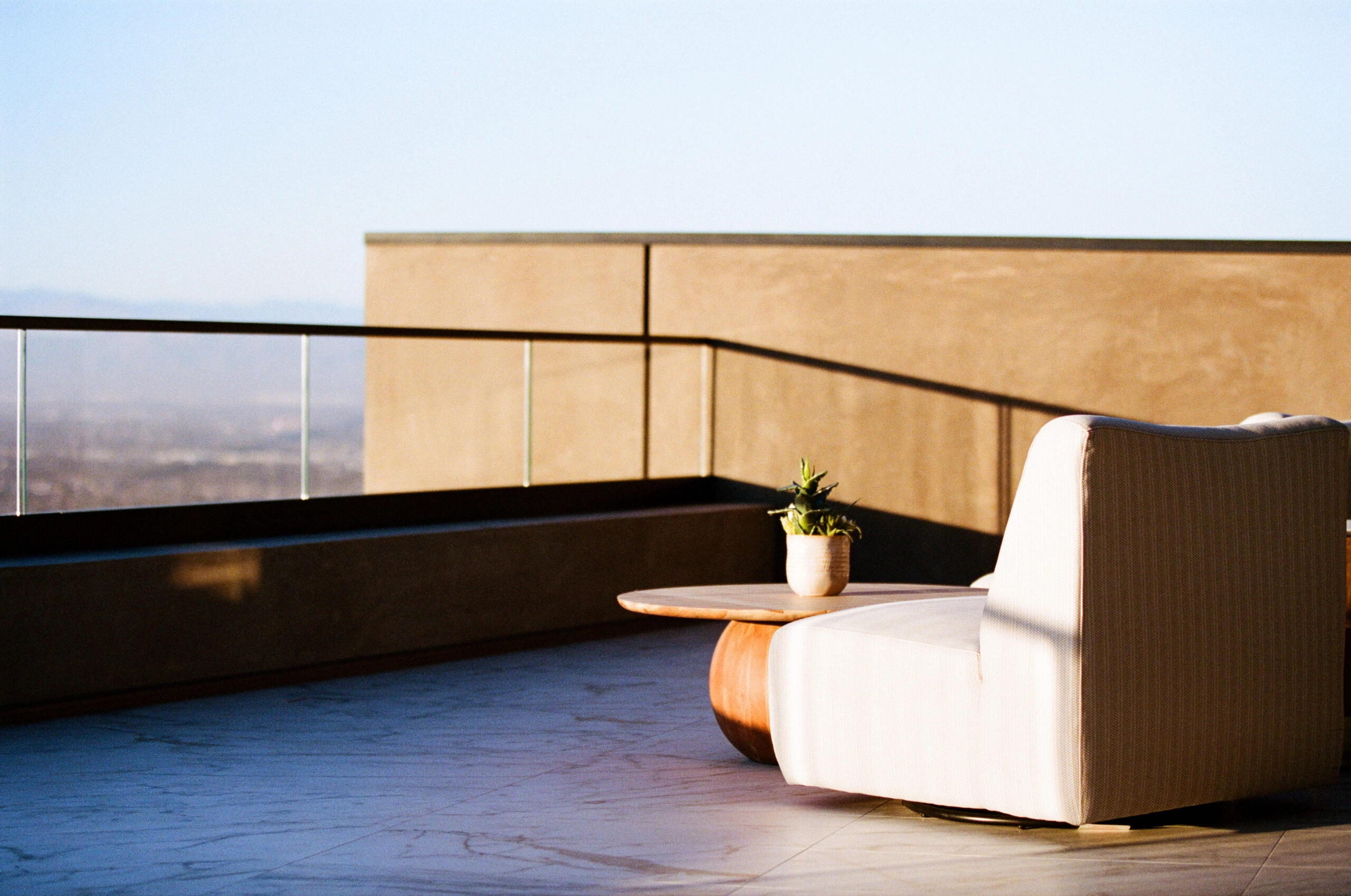 A wood-capped glass railing encloses a rooftop terrace with lounge seating at dusk