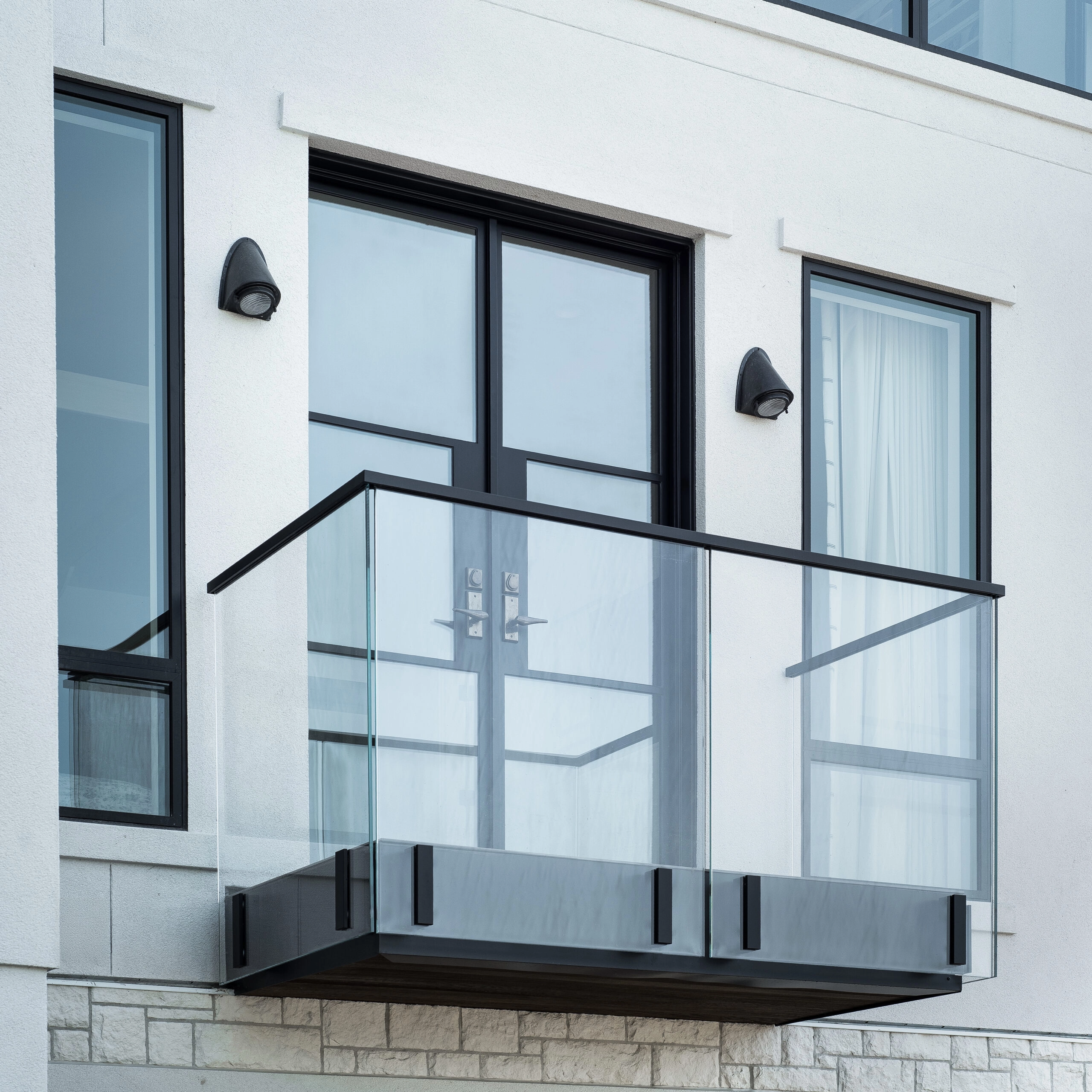 Side-mounted glass railing wraps a black steel balcony on a white exterior