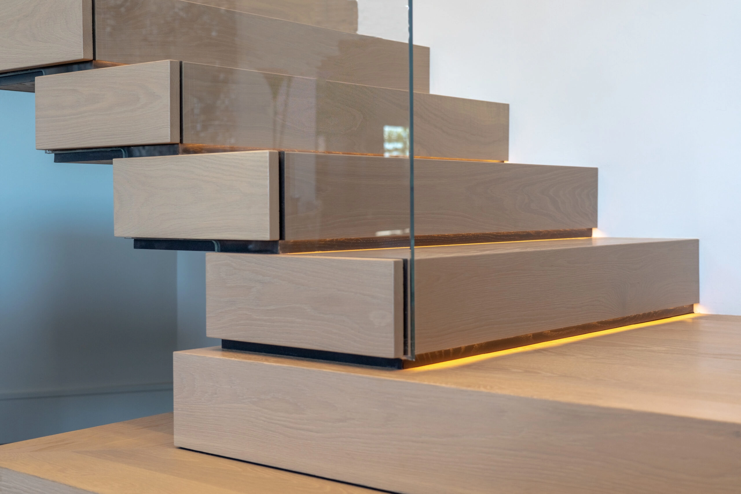 Close-up of stacked treads meeting a glass panel above a lit bottom step