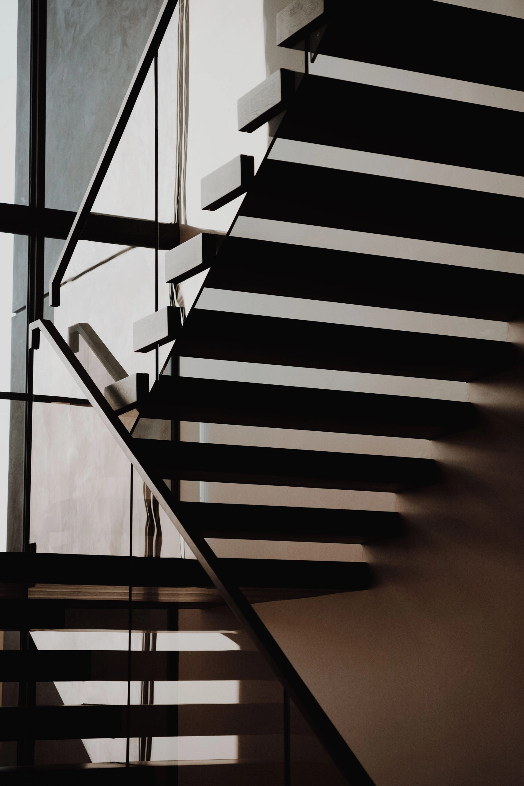 A switchback cantilever stair casts long shadows across a dim entry wall
