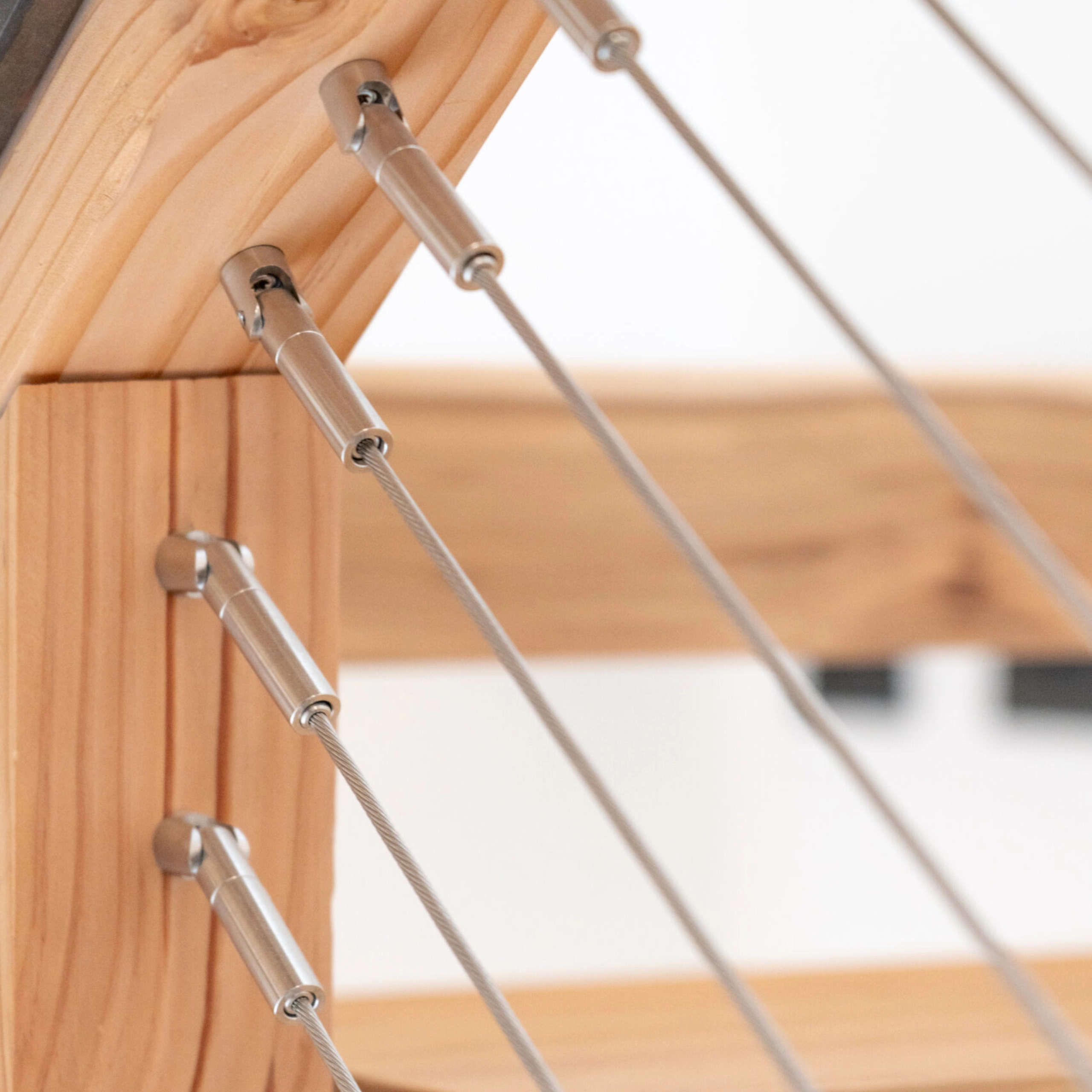 Angled cable lines leave a wood stair post through polished metal fittings