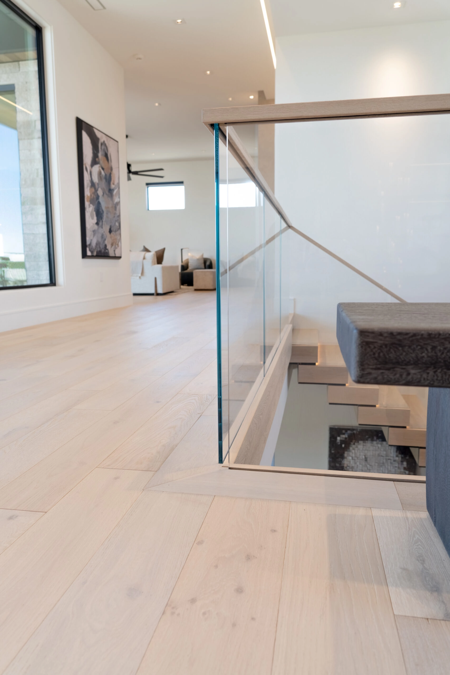 Glass railing with a wood cap guards an upstairs hall above the stairwell