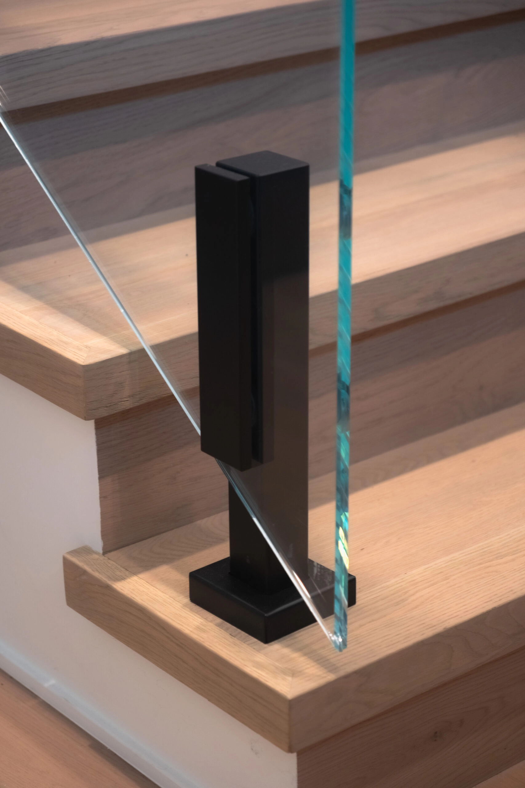 Close-up of a black spigot clamping a glass panel beside floating stair treads