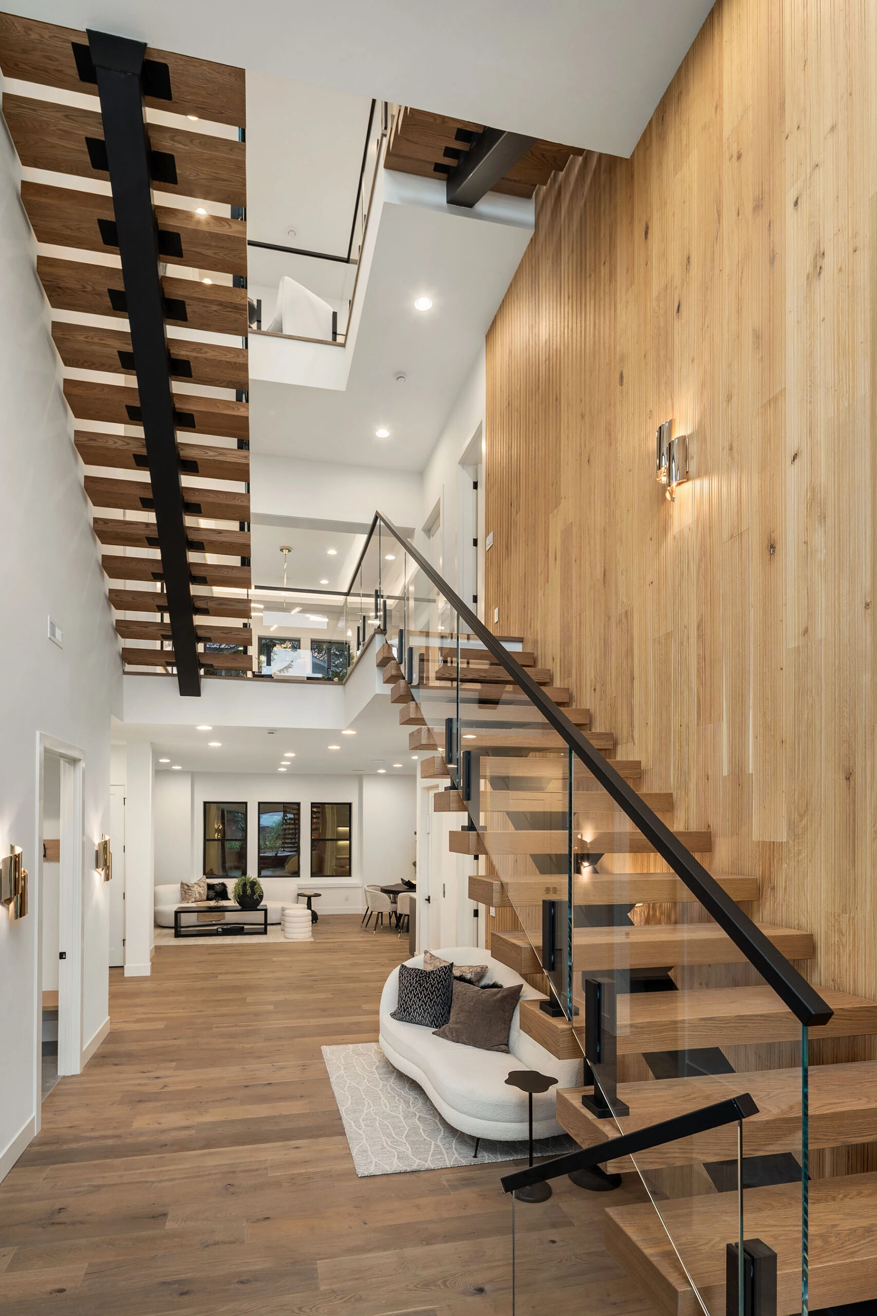 Open living space where a floating stair descends past a full-height wood wall